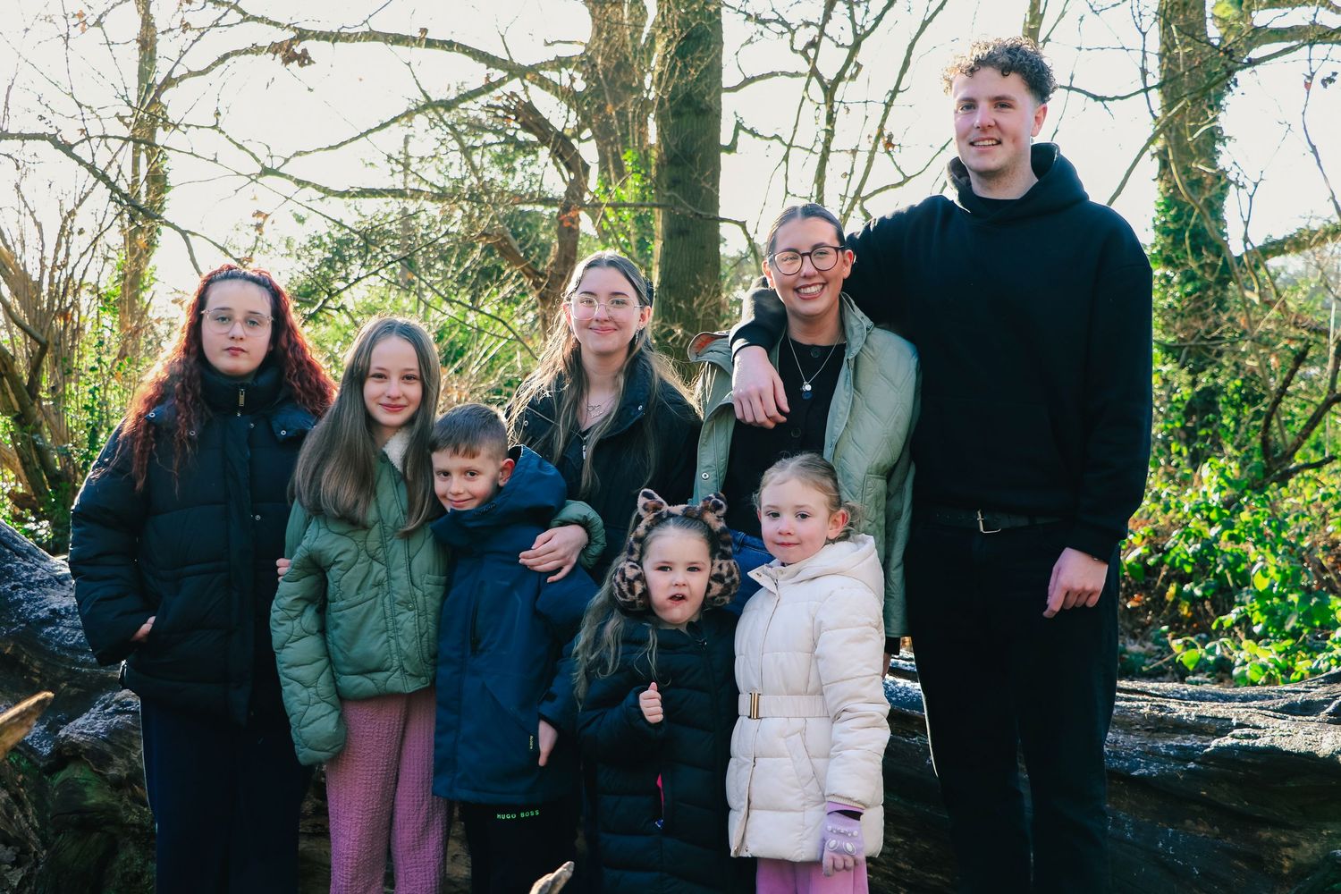 A group of people stand together outdoors on a winter day surrounded by bare trees and natural scenery.