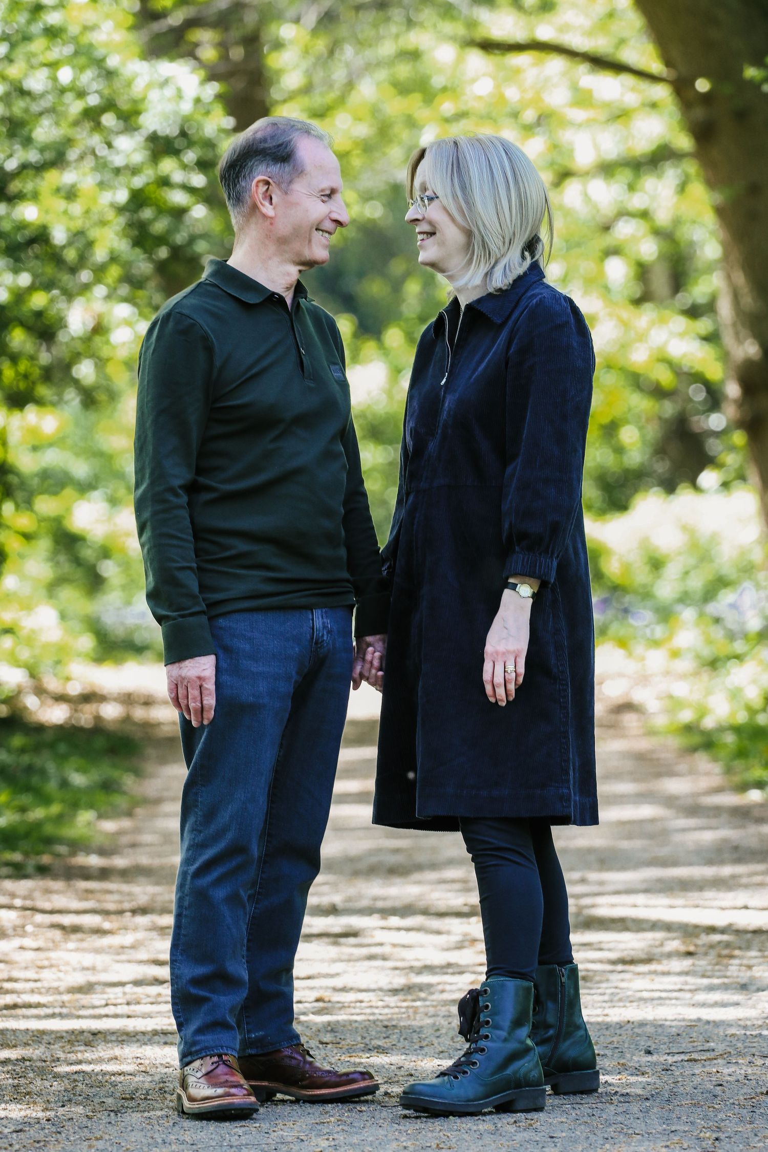 Two people in dark clothing share a joyful moment while standing together on a sunlit path in a park setting.