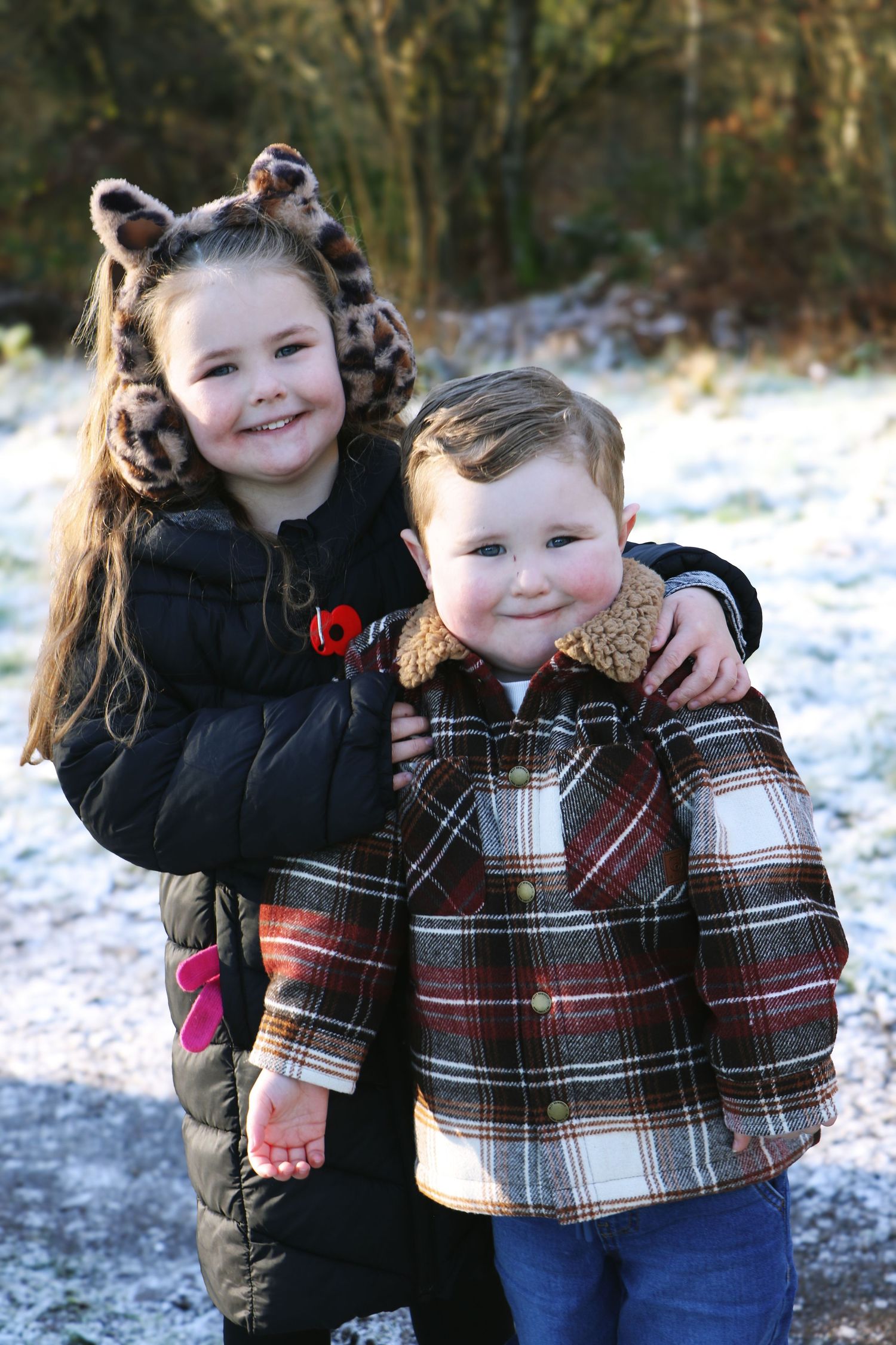 Two children in winter clothing embrace and laugh together while playing in the snow.