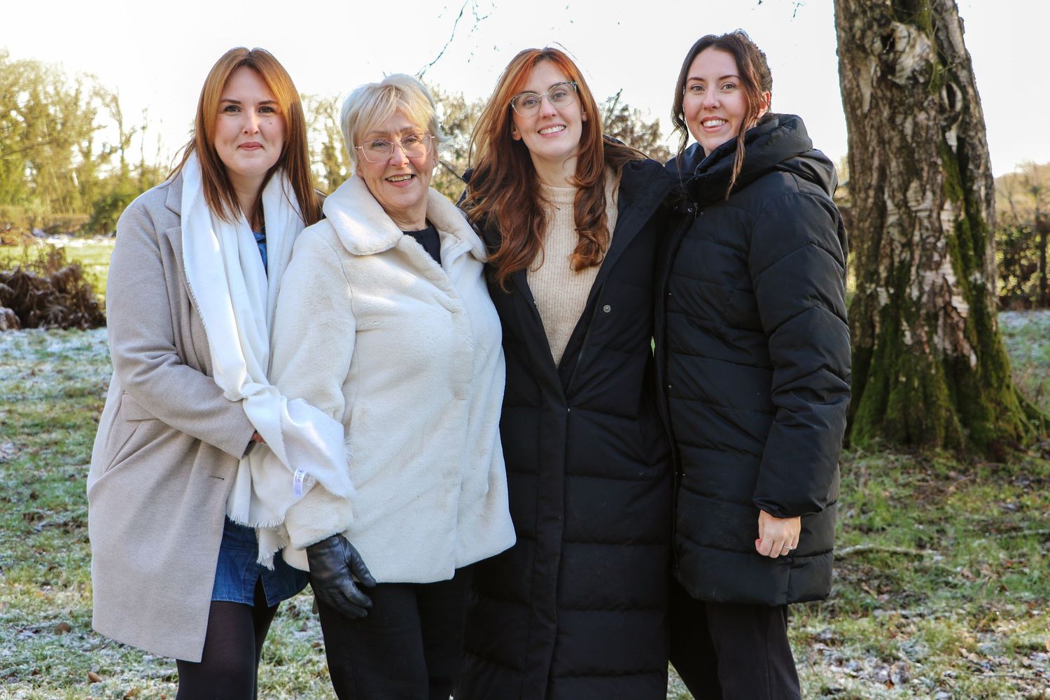 A group of people in casual winter attire smiling together outdoors on a sunny autumn day.