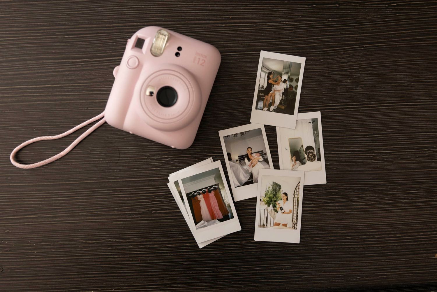 Pink Instax mini camera with vintage polaroid photos displayed on dark wooden surface.