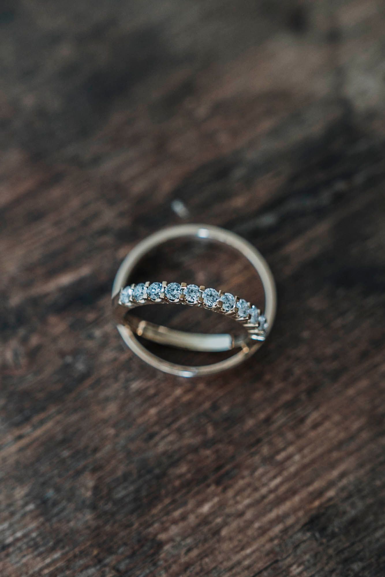 Diamond wedding ring with sparkling stones photographed on rustic wooden surface.