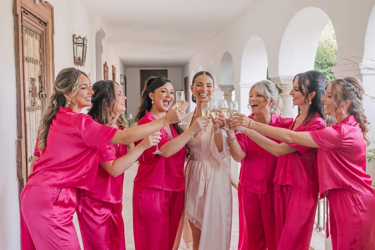 Celebratory toast with bridal party wearing bright pink matching outfits.