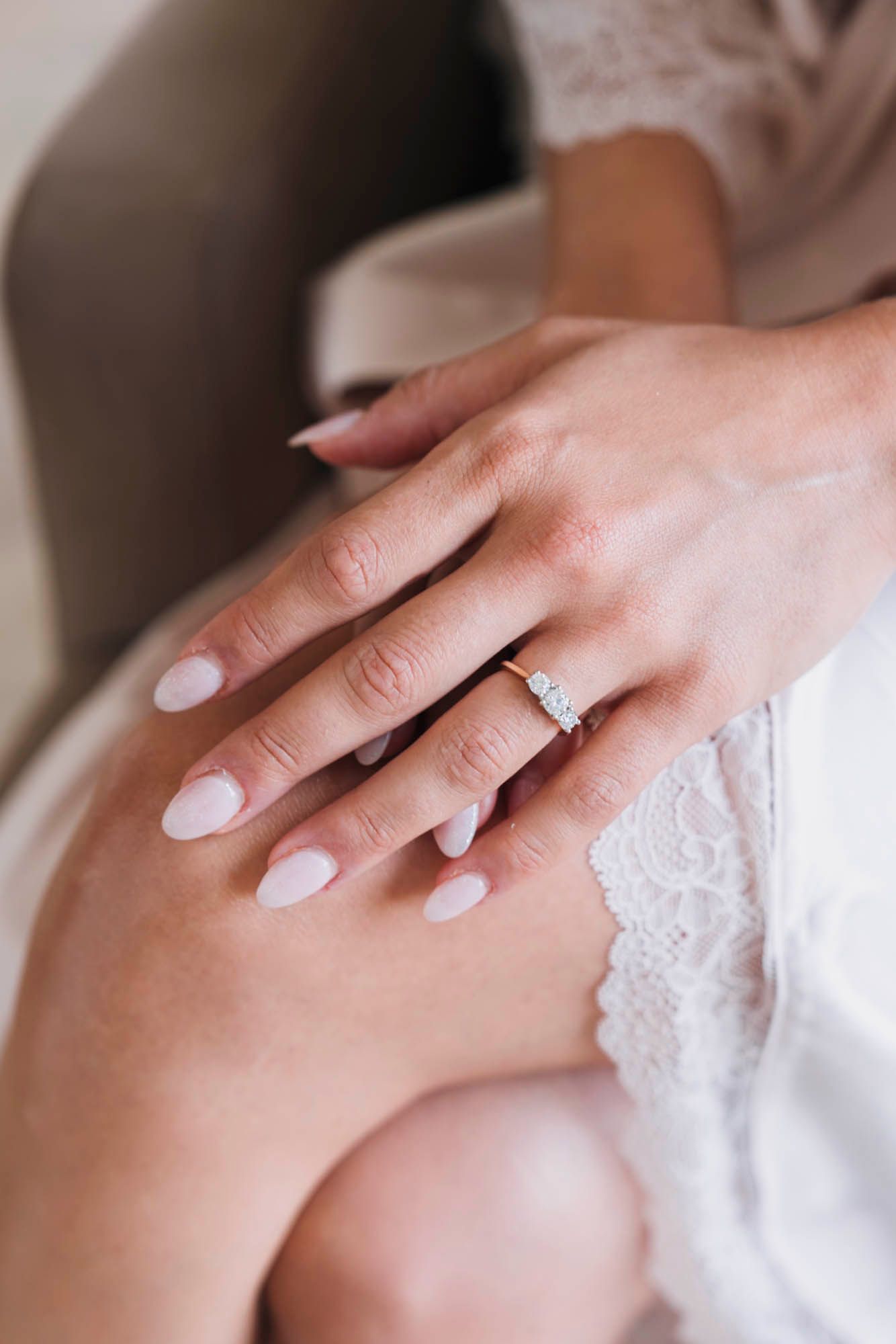 Close-up of manicured hands with engagement ring and lace details on white robe.