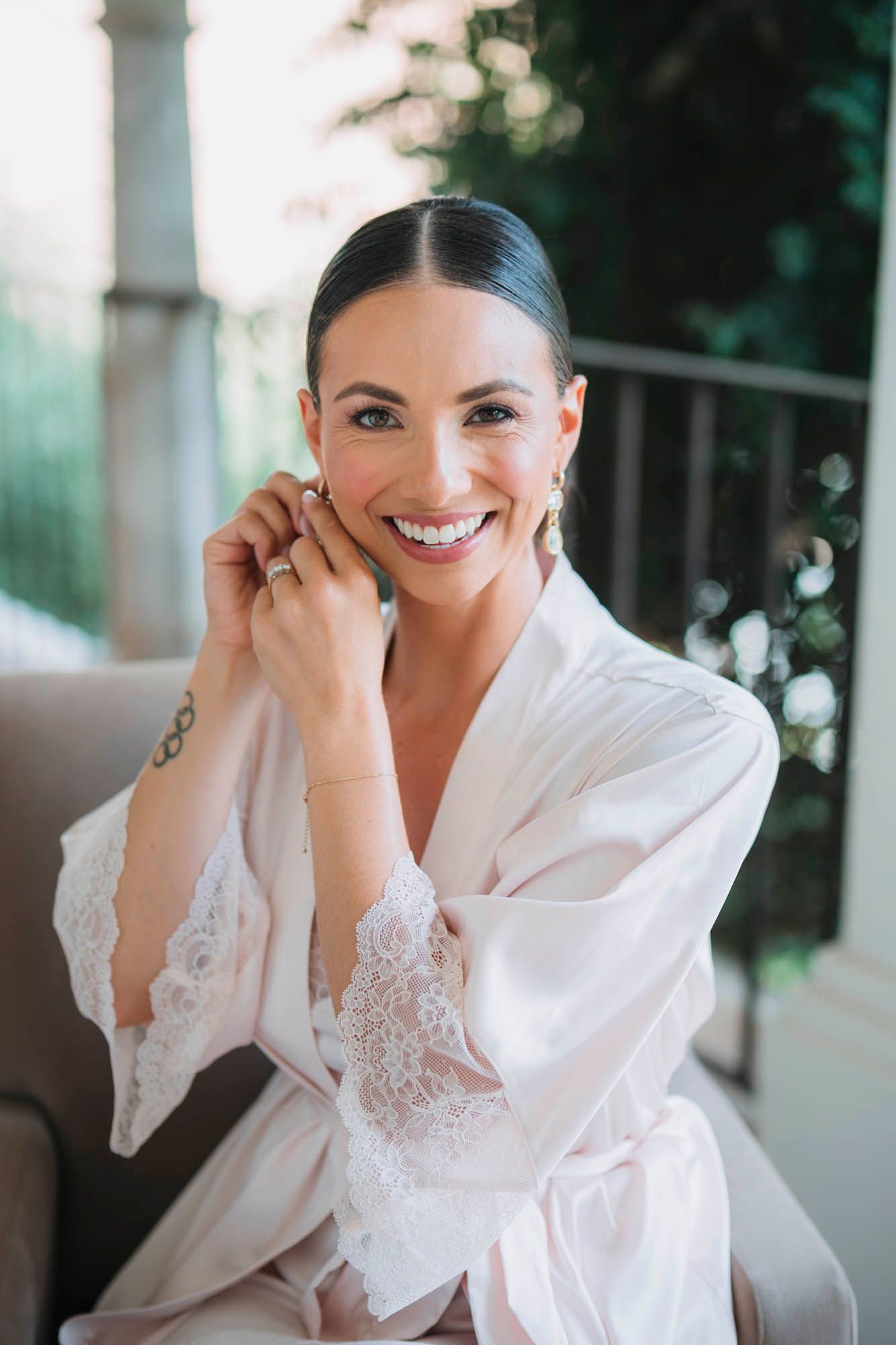 Person in white lace robe smiles joyfully during wedding morning preparations.