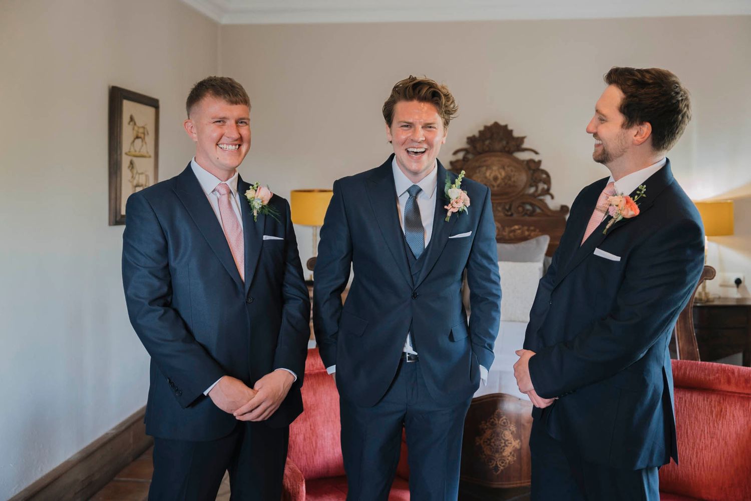 Three people in suits share a laugh together in elegant room with red couch.