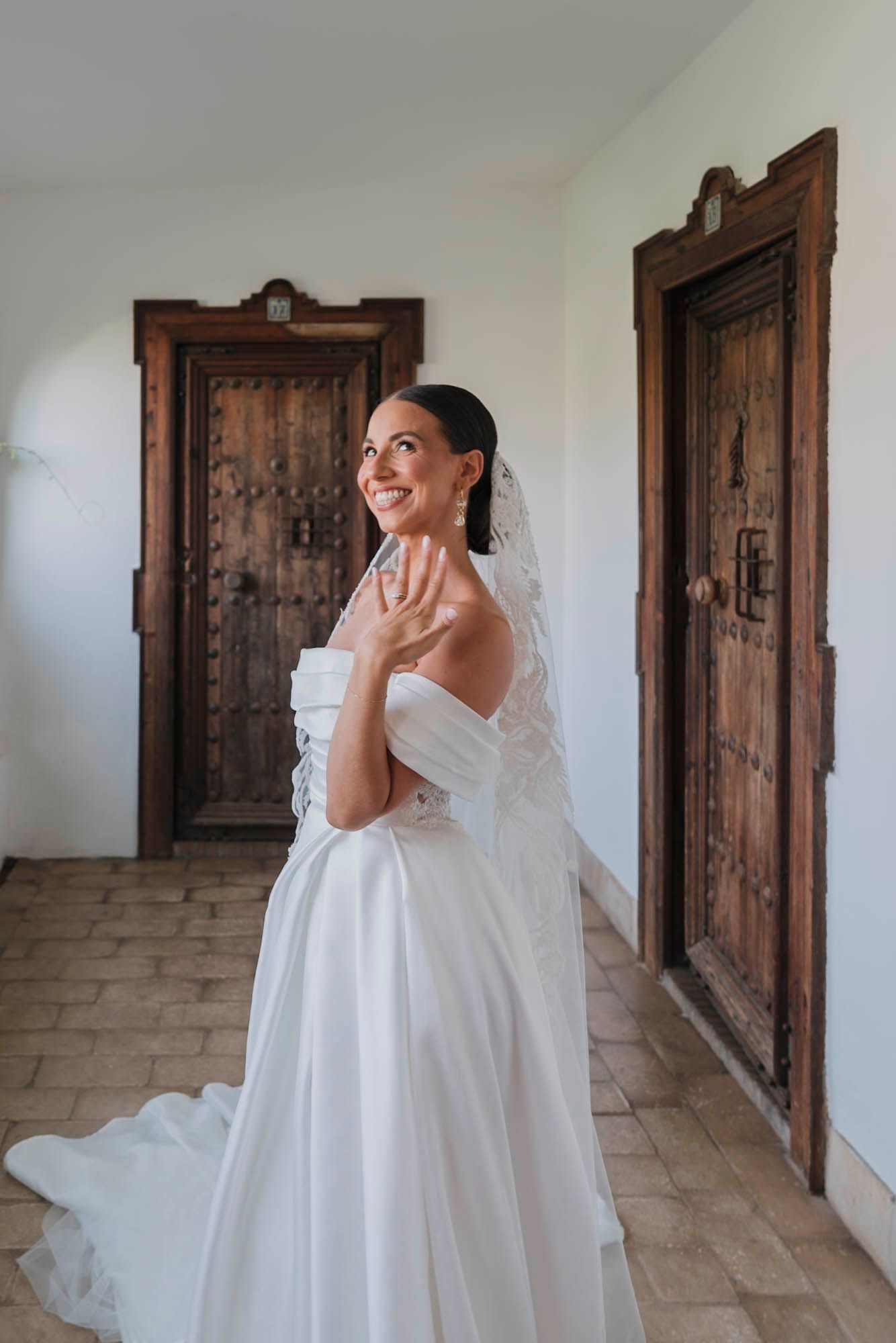 Elegant bride in a white strapless gown laughs joyfully in a hallway with rustic wooden doors.