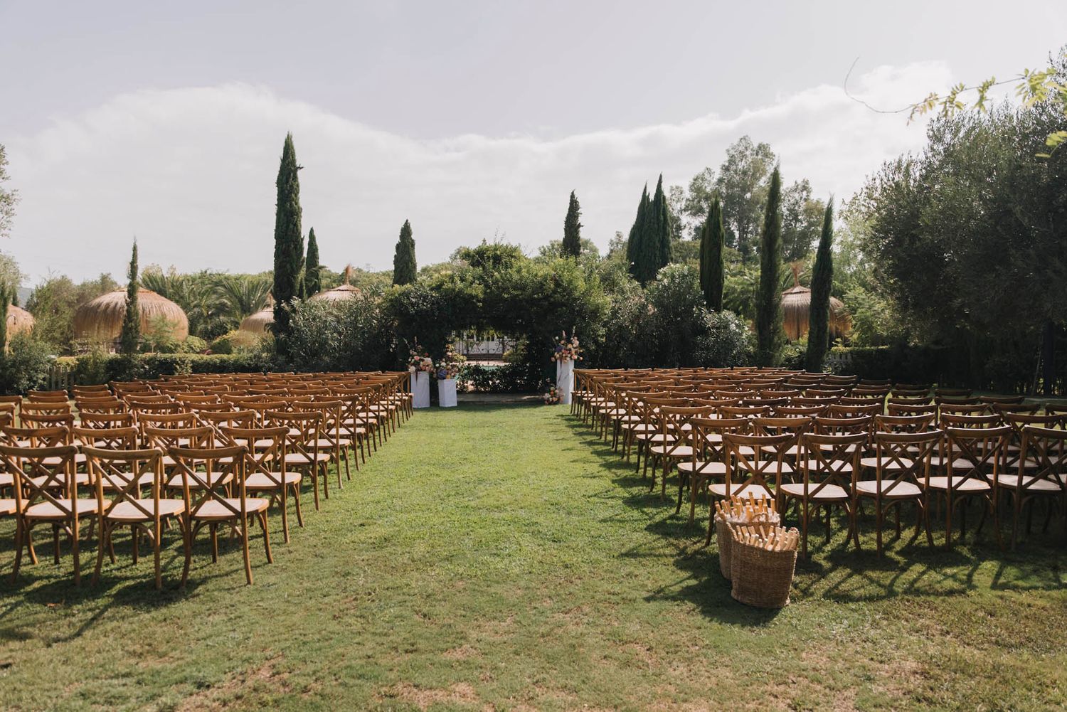 Outdoor wedding ceremony setup with wooden chairs lined up on grass facing cypress trees.