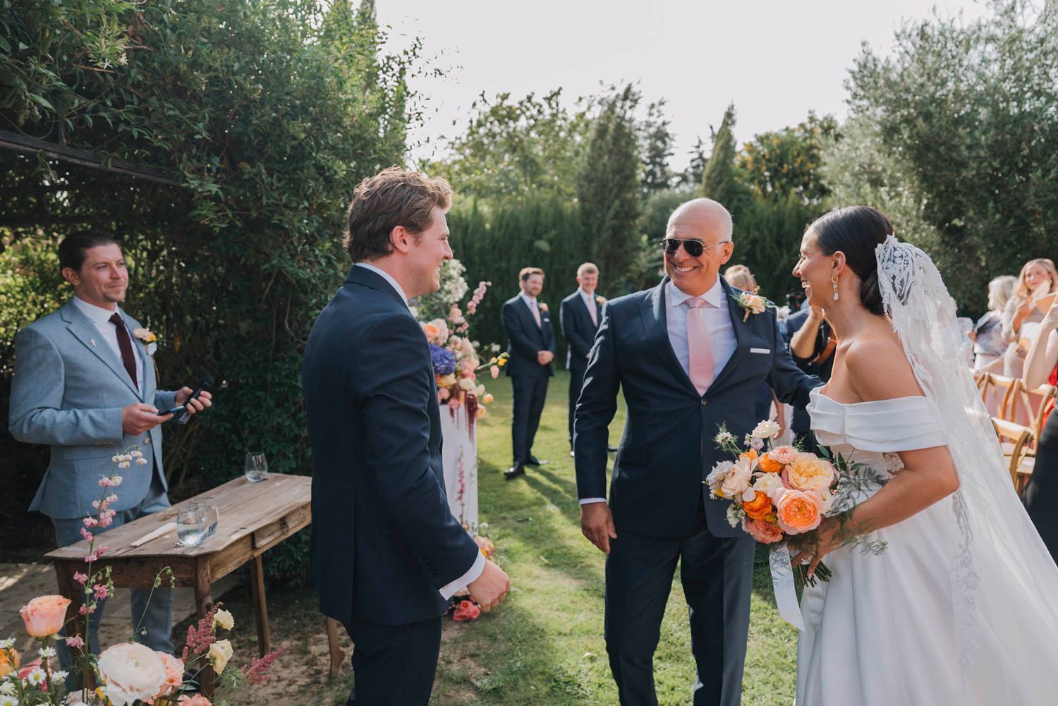 Wedding celebration in an outdoor garden setting with rustic wooden furniture.