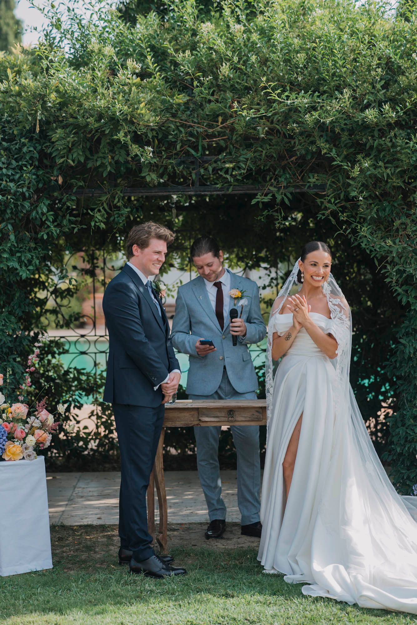 Wedding ceremony under a natural green archway with floral decorations.