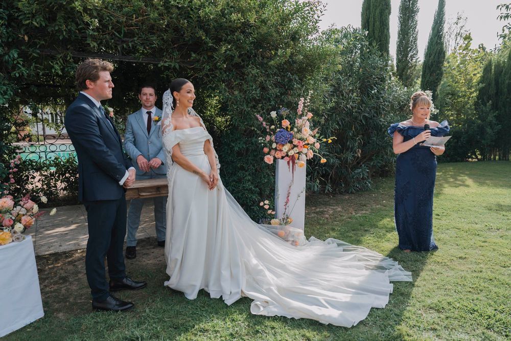 Outdoor garden wedding ceremony with flowing white dress and floral arrangements.