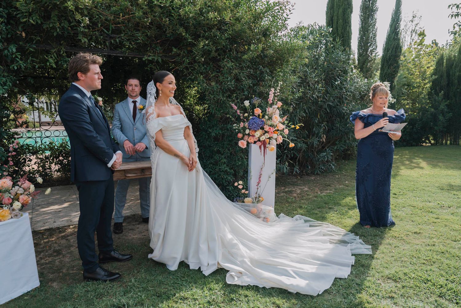 Outdoor garden wedding ceremony with flowing white dress and floral arrangements.