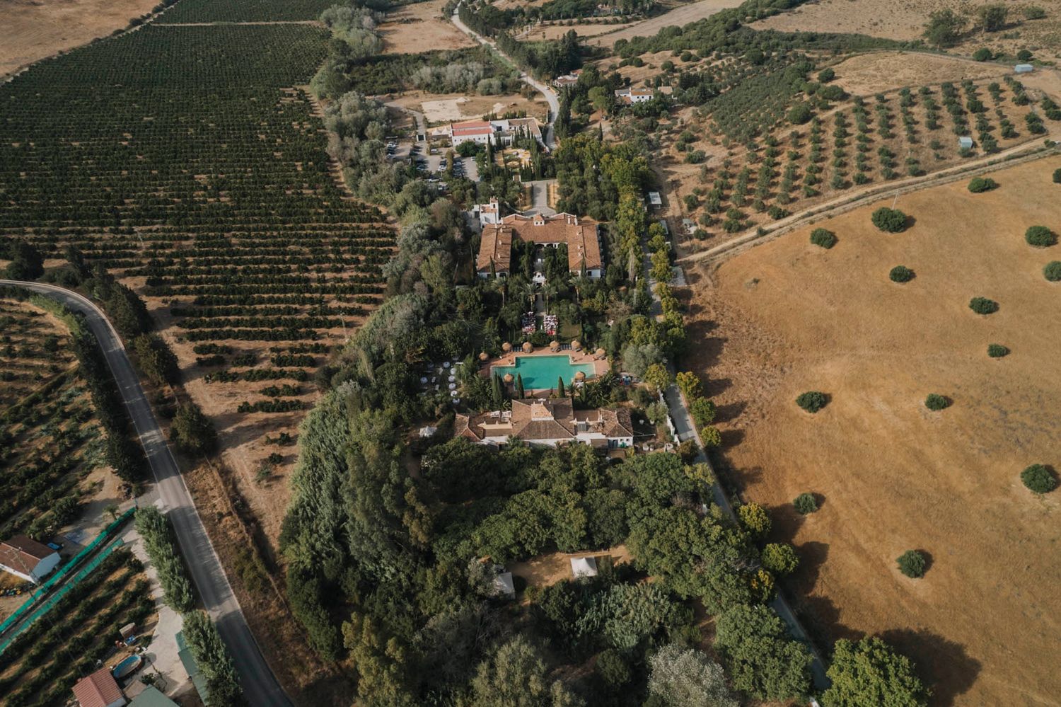 Aerial view of a luxurious Tuscan villa estate with swimming pool surrounded by olive groves and cypress trees.