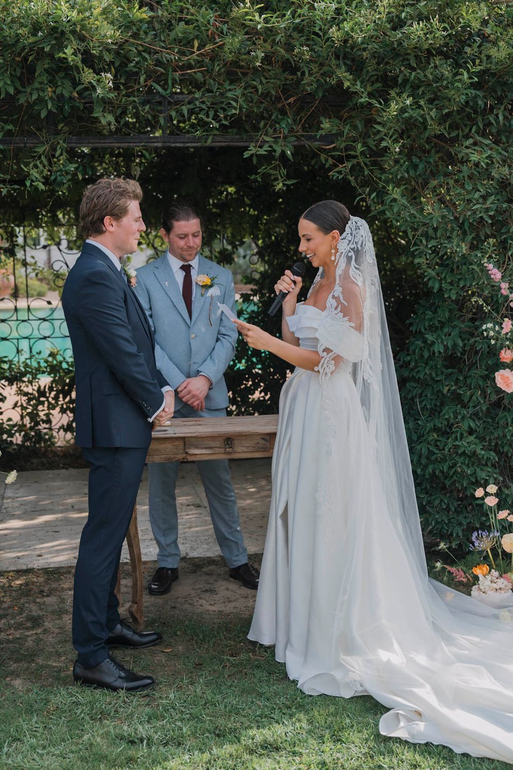 Wedding ceremony taking place under a lush garden archway with formal attire and traditional decor.