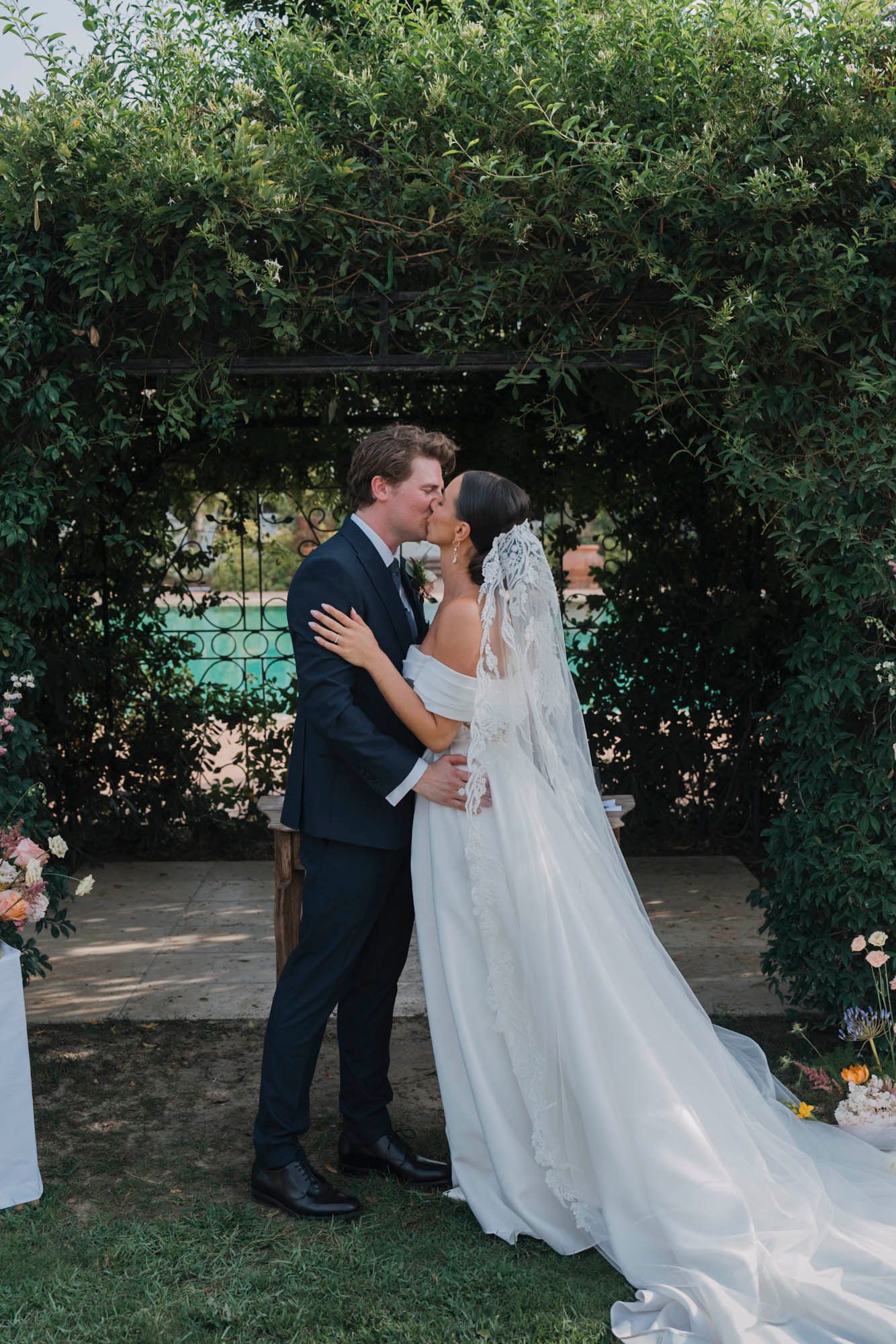 Romantic wedding kiss under a garden archway with flowing white dress and veil.