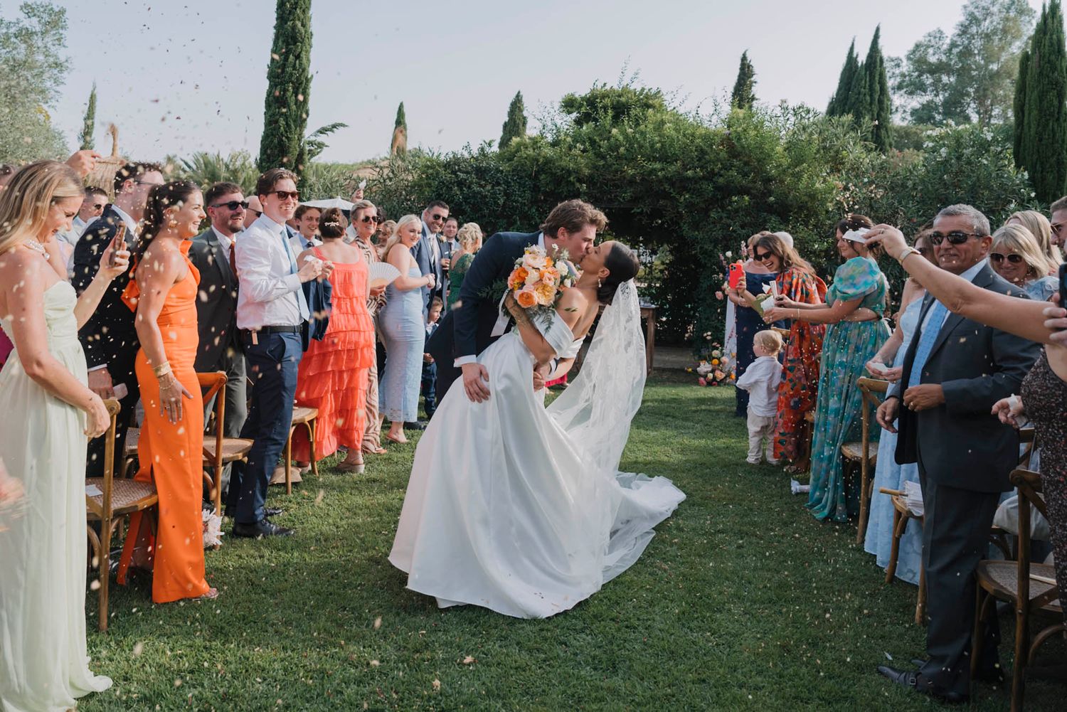 Celebration moment with guests tossing confetti on garden pathway during wedding exit.
