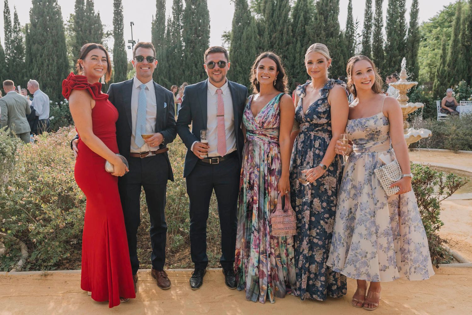 Wedding party members pose in formal attire against a garden backdrop.