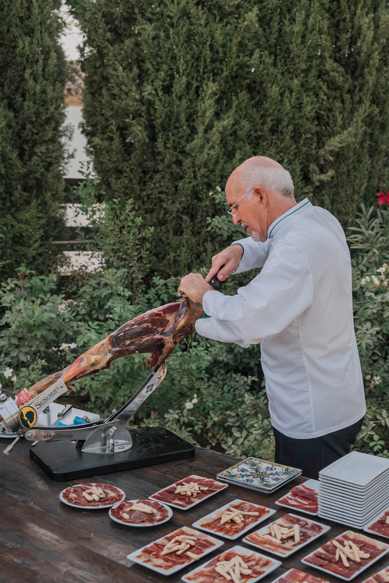 Chef carving a leg of meat at an outdoor wedding catering station.