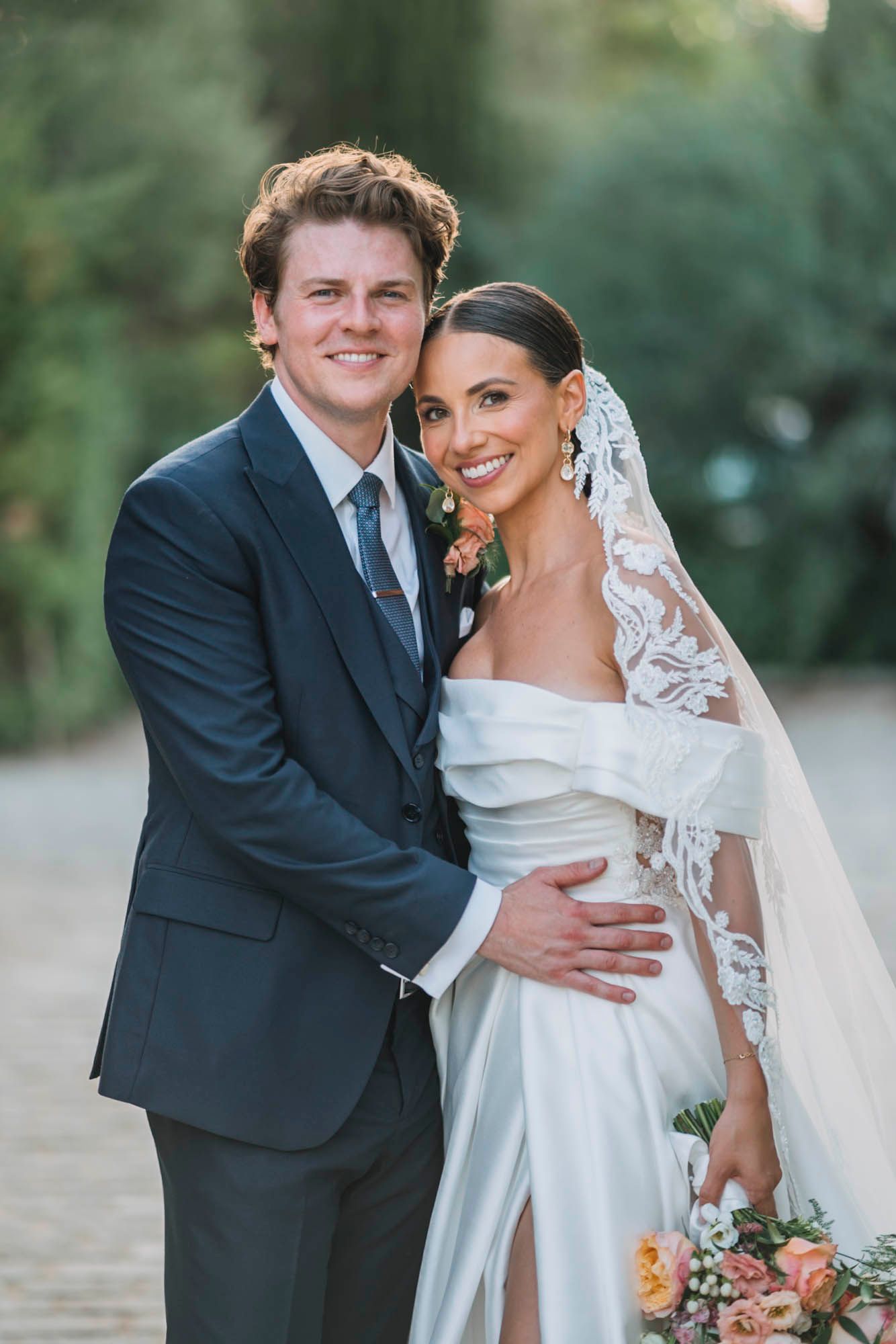 Elegant wedding portrait featuring couple in formal attire with bride holding peach bouquet.