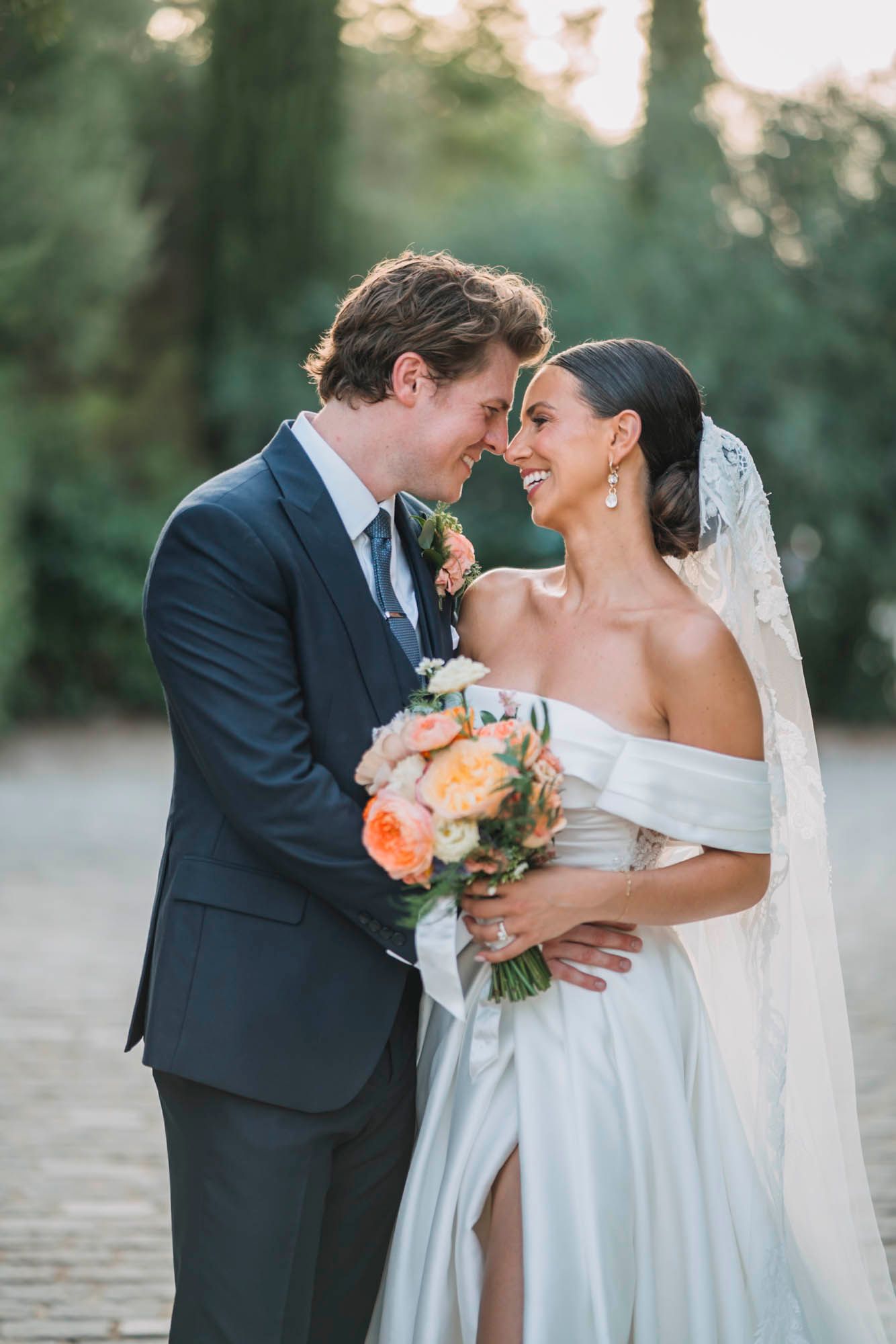 Intimate wedding portrait of couple sharing romantic moment with peach bouquet.