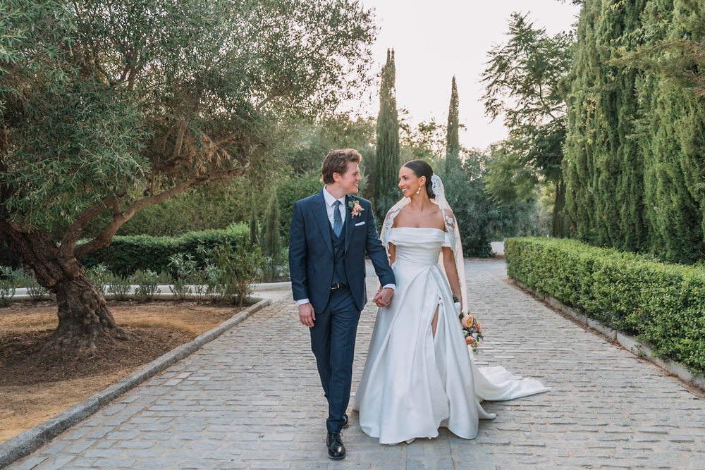 Newlywed couple walking together on stone path surrounded by lush garden scenery.