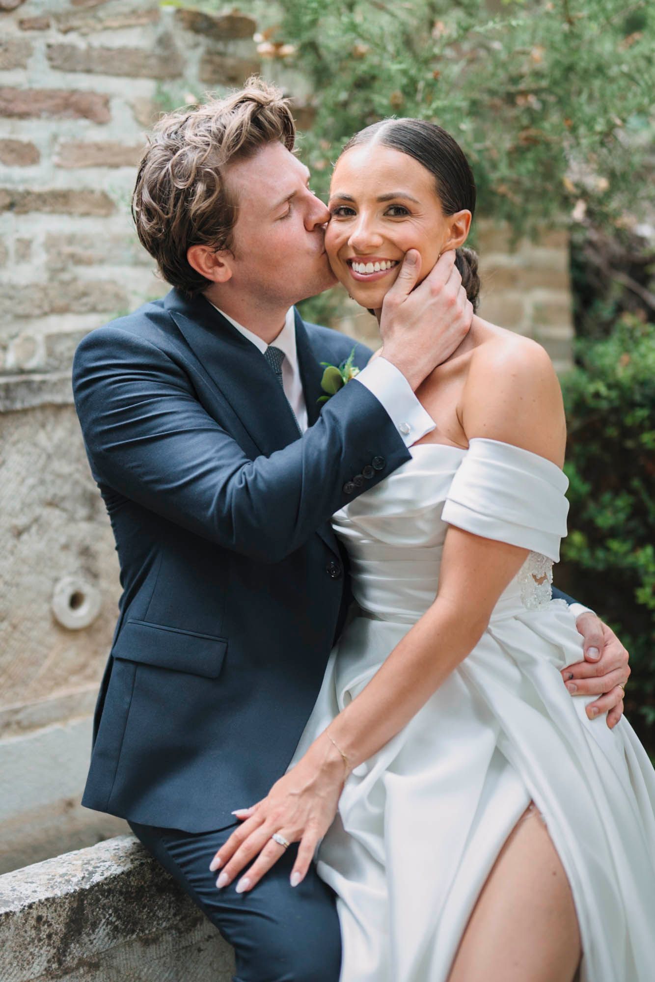 Romantic moment captured between newlyweds against stone wall backdrop.