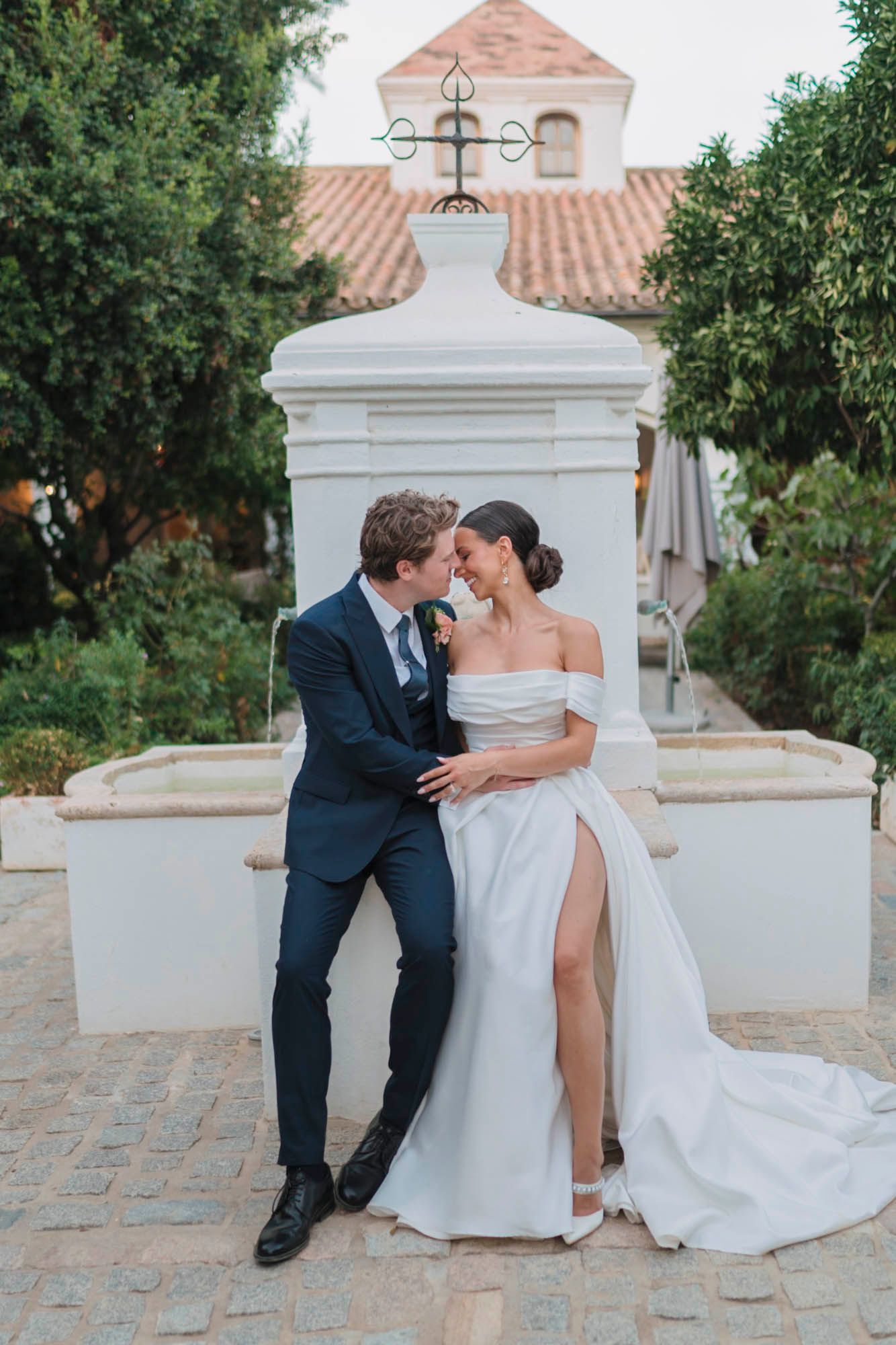A romantic wedding moment captured in front of a white mission-style church with terracotta roof tiles.