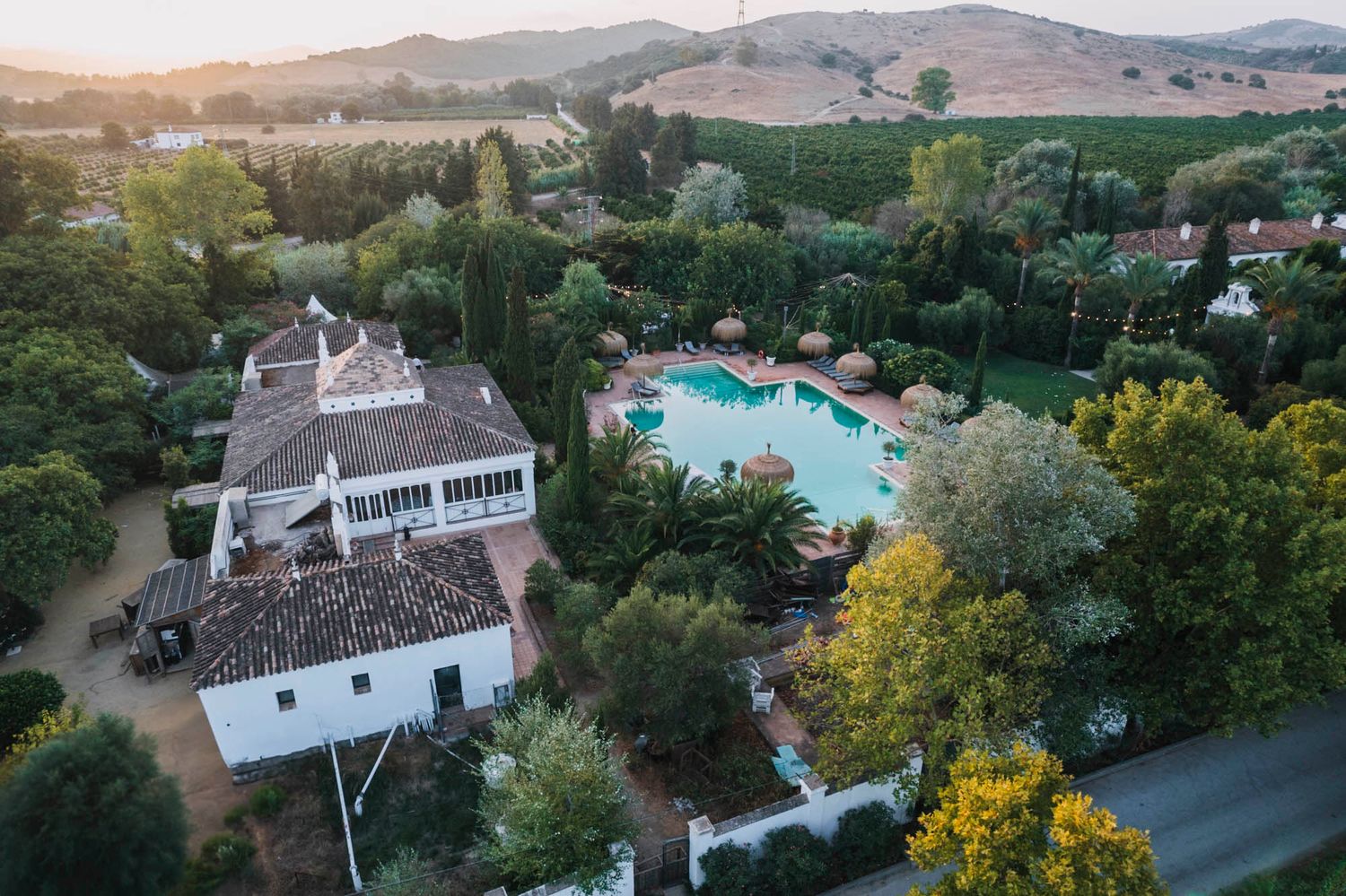 Aerial view of a luxury resort venue with swimming pool and white buildings nestled among rolling hills.