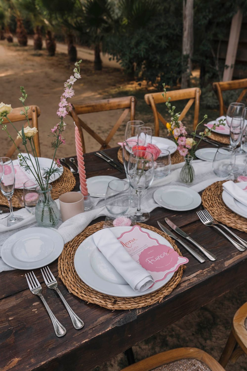 Close-up of rustic wedding place setting with woven charger plate and pink menu card.