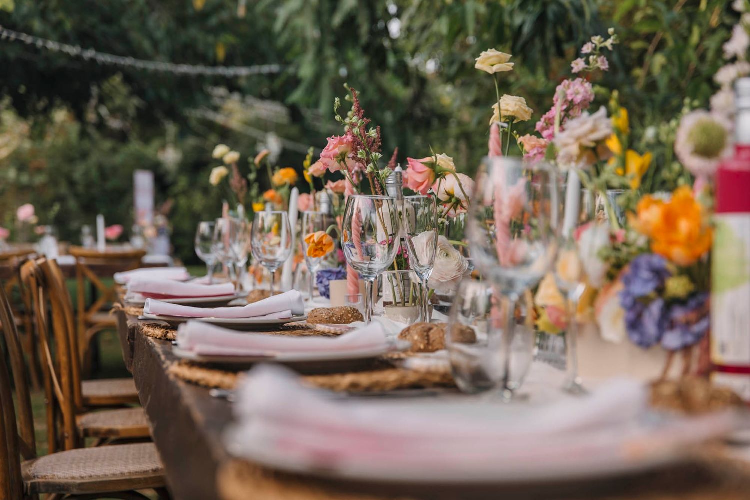 Romantic table setting with delicate floral arrangements and vintage glassware at outdoor reception.