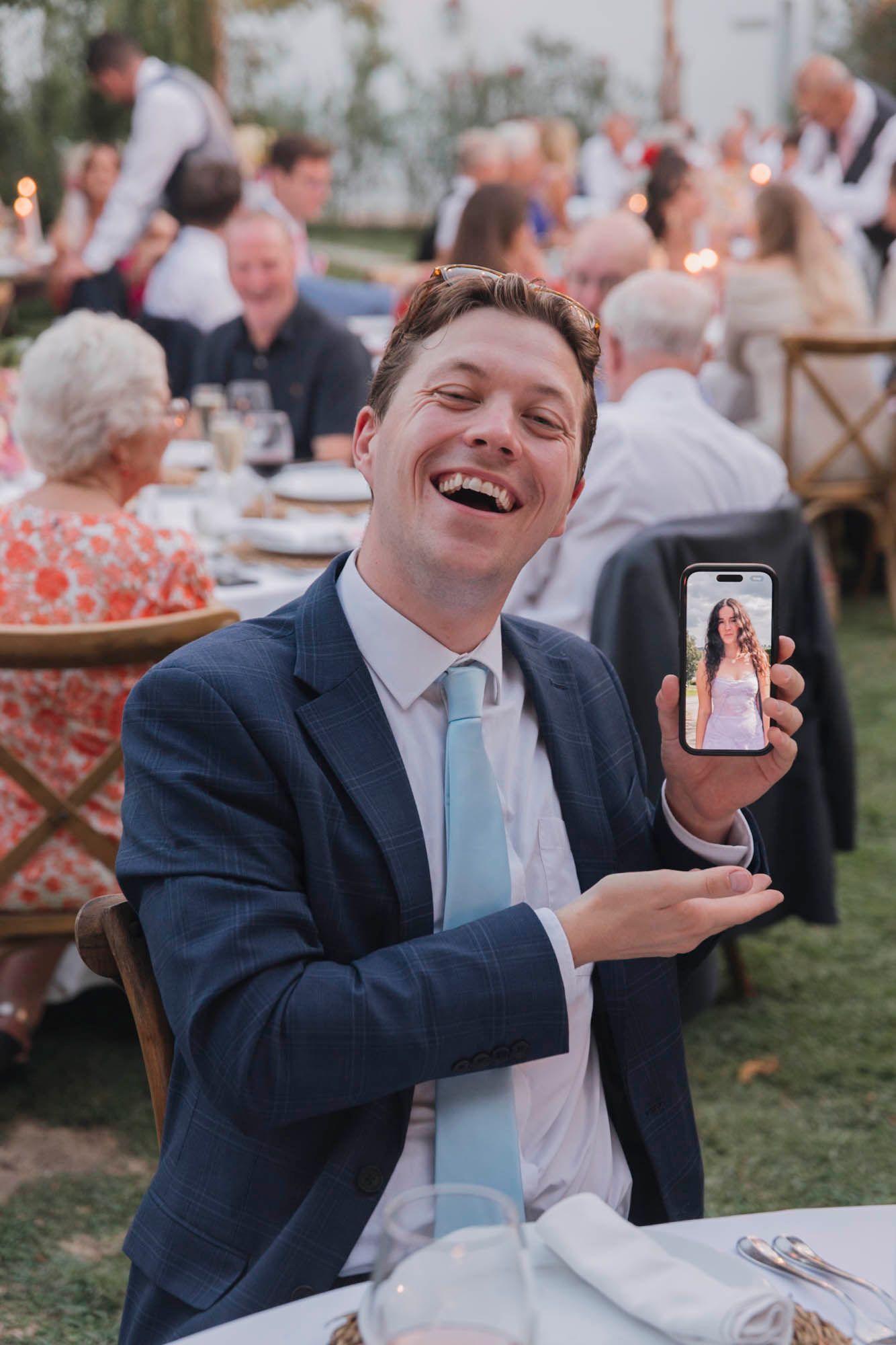 Guest enjoying the outdoor wedding reception while showing phone screen at dinner table.