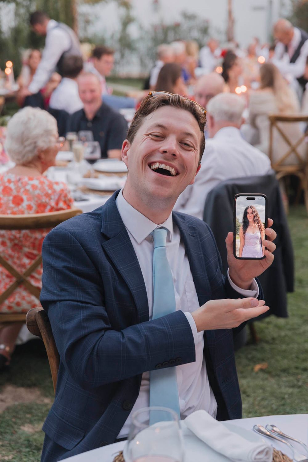 Guest enjoying the outdoor wedding reception while showing phone screen at dinner table.