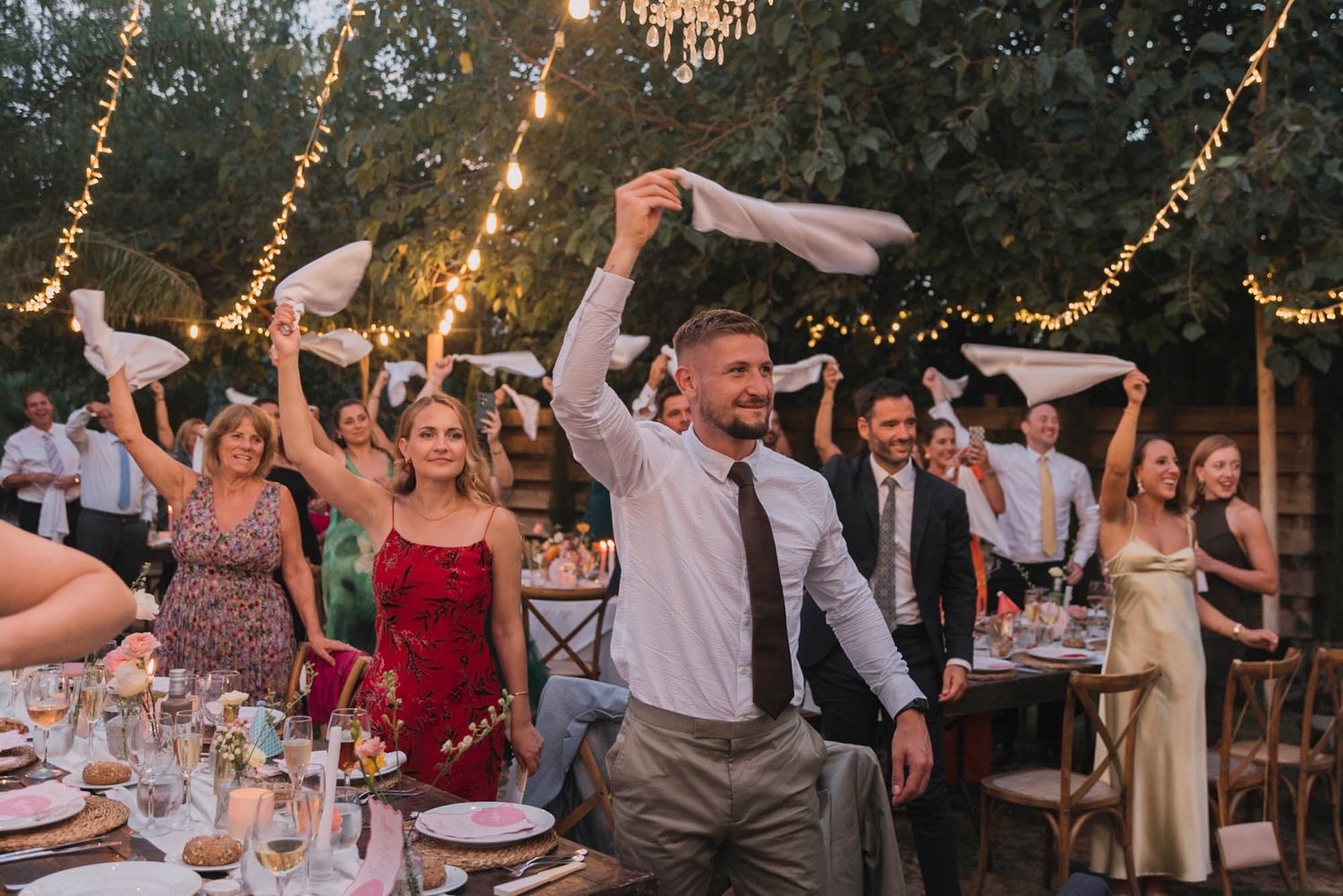 Wedding guests dancing and celebrating under string lights at an outdoor reception.