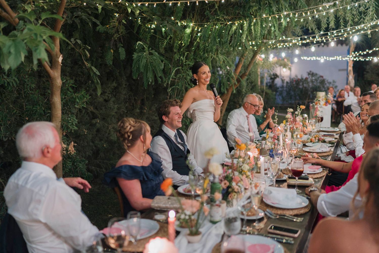 Guests enjoy dinner at long tables during an outdoor evening wedding reception.