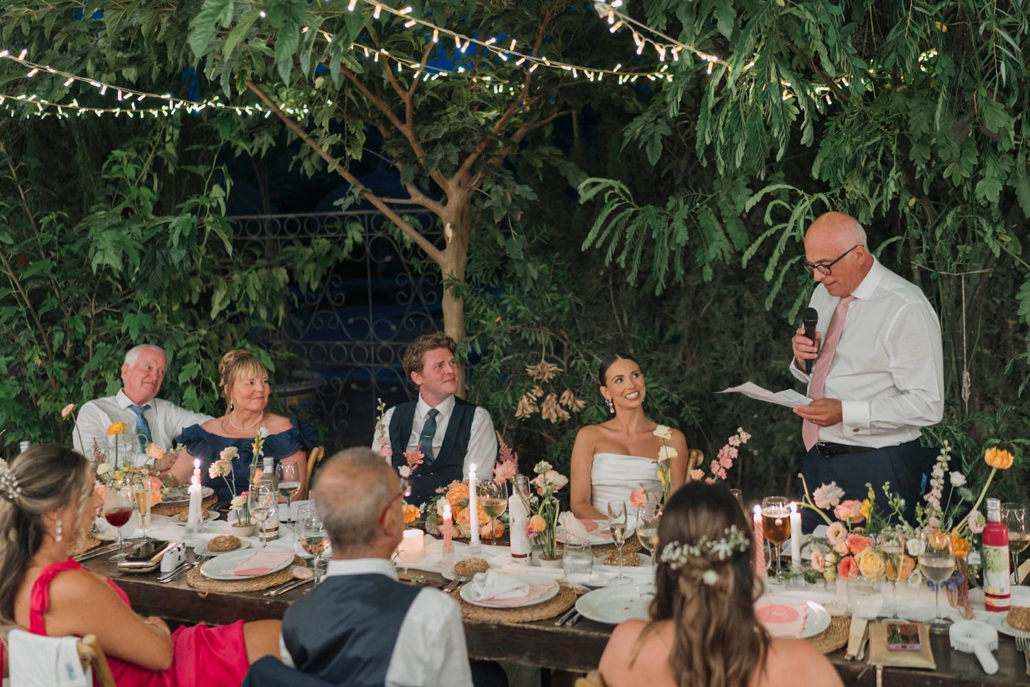 Wedding reception dinner party under string lights with guests seated at decorated tables.