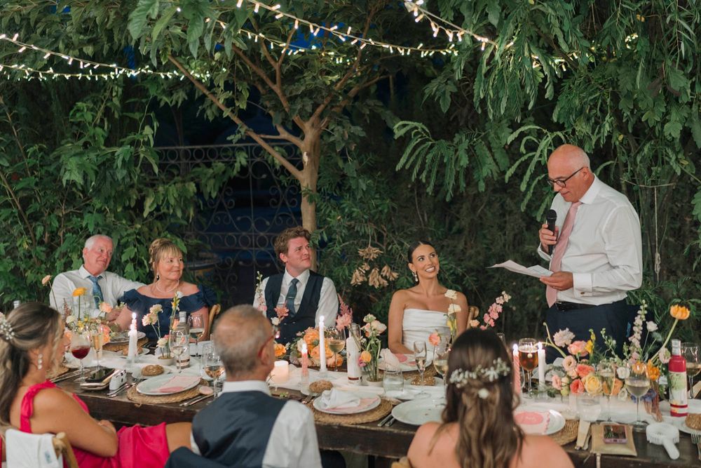 Wedding reception dinner party under string lights with guests seated at decorated tables.