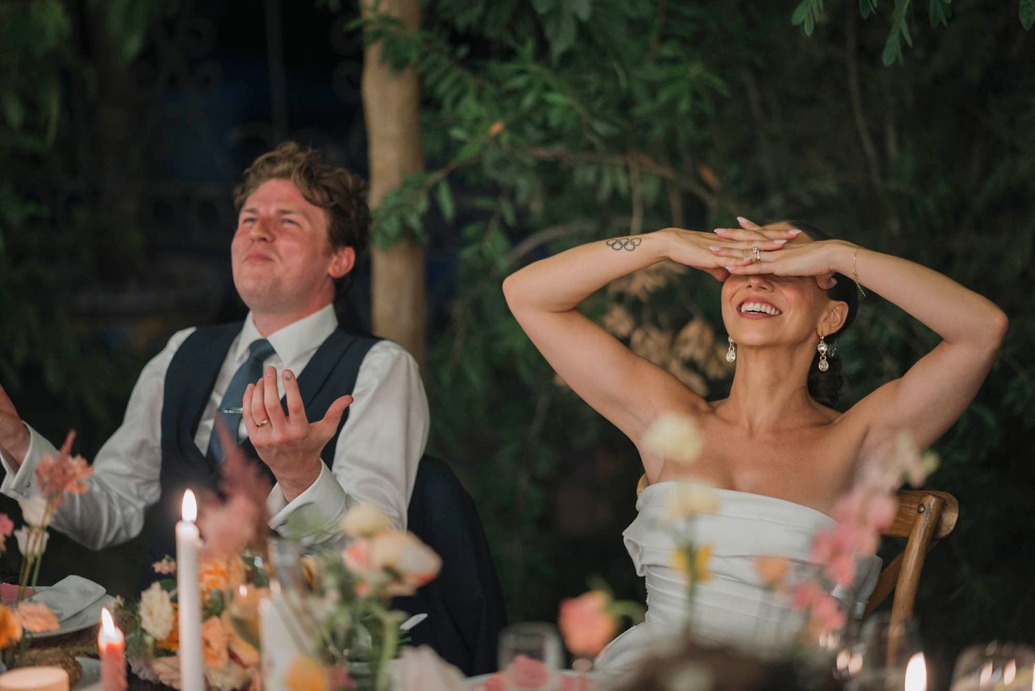 At a candlelit outdoor reception, a couple reacts joyfully during emotional wedding toasts.