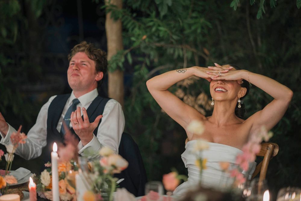 At a candlelit outdoor reception, a couple reacts joyfully during emotional wedding toasts.