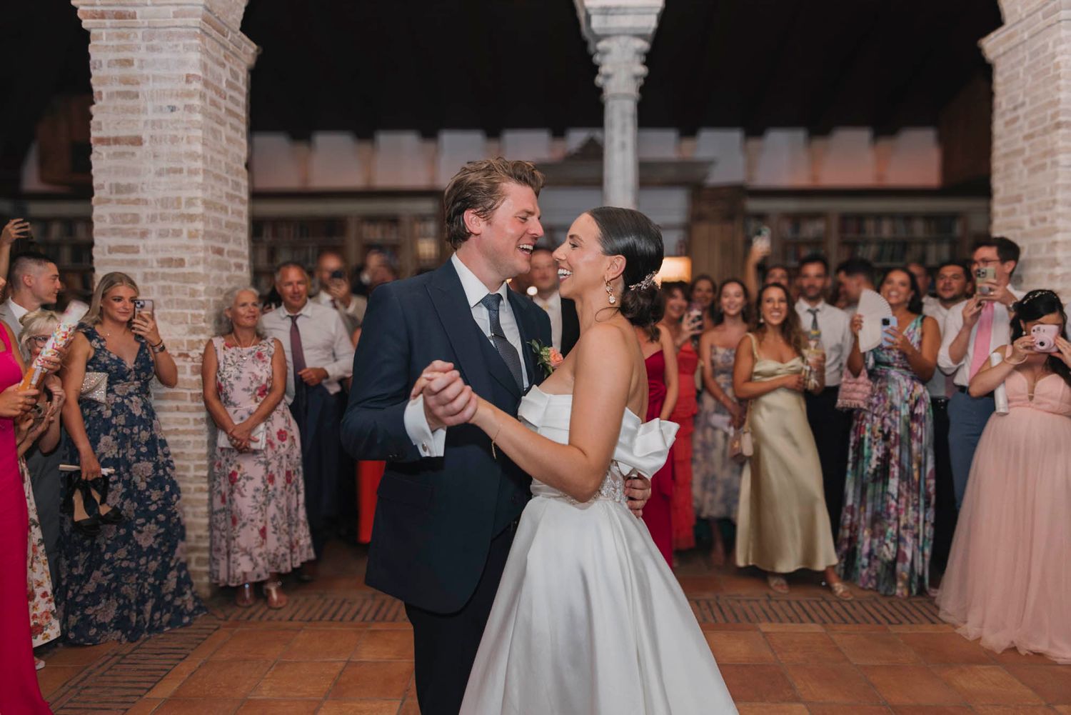 A couple shares their first dance surrounded by guests in an elegant arched venue.
