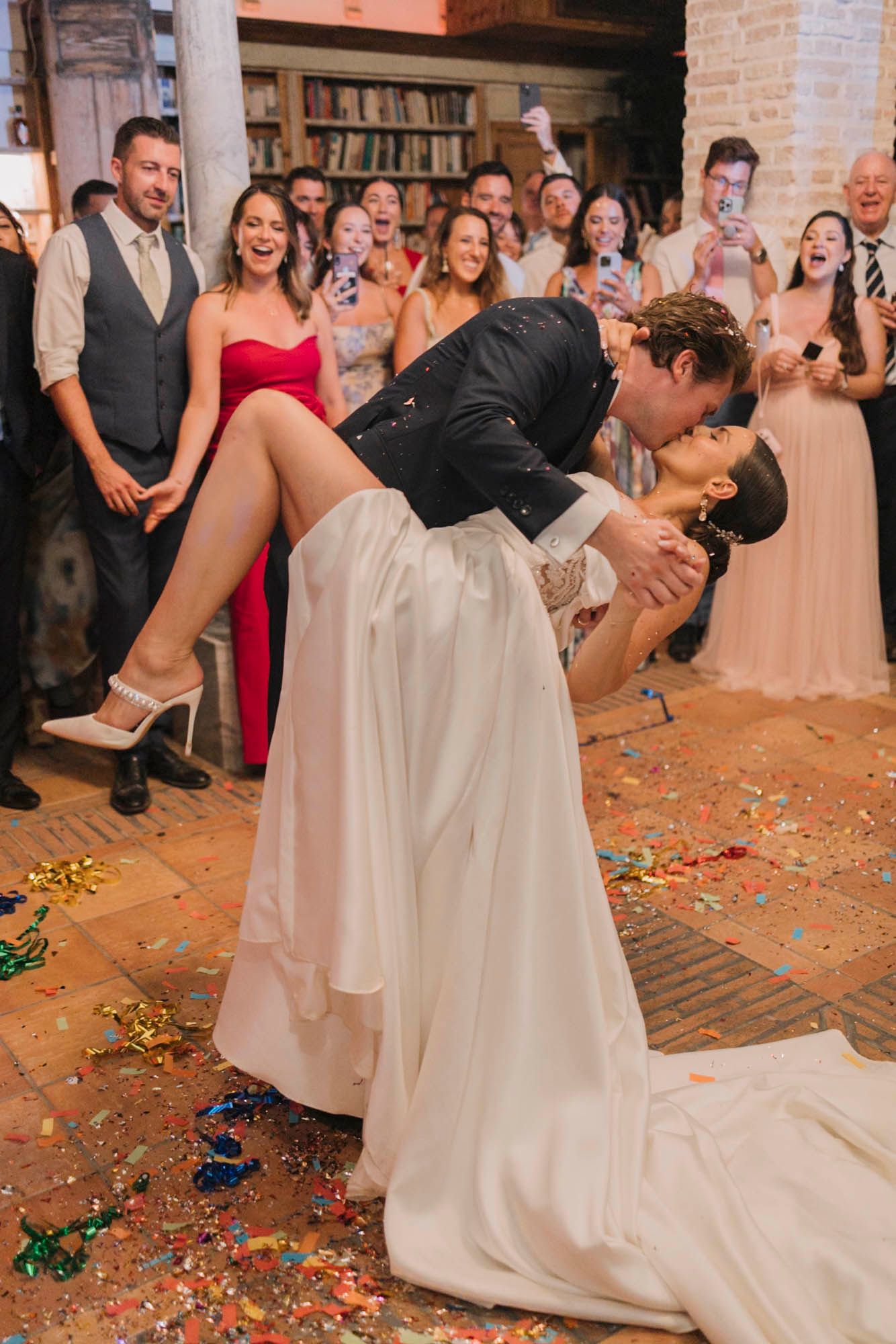 A romantic dip dance move surrounded by cheering wedding guests and scattered confetti.