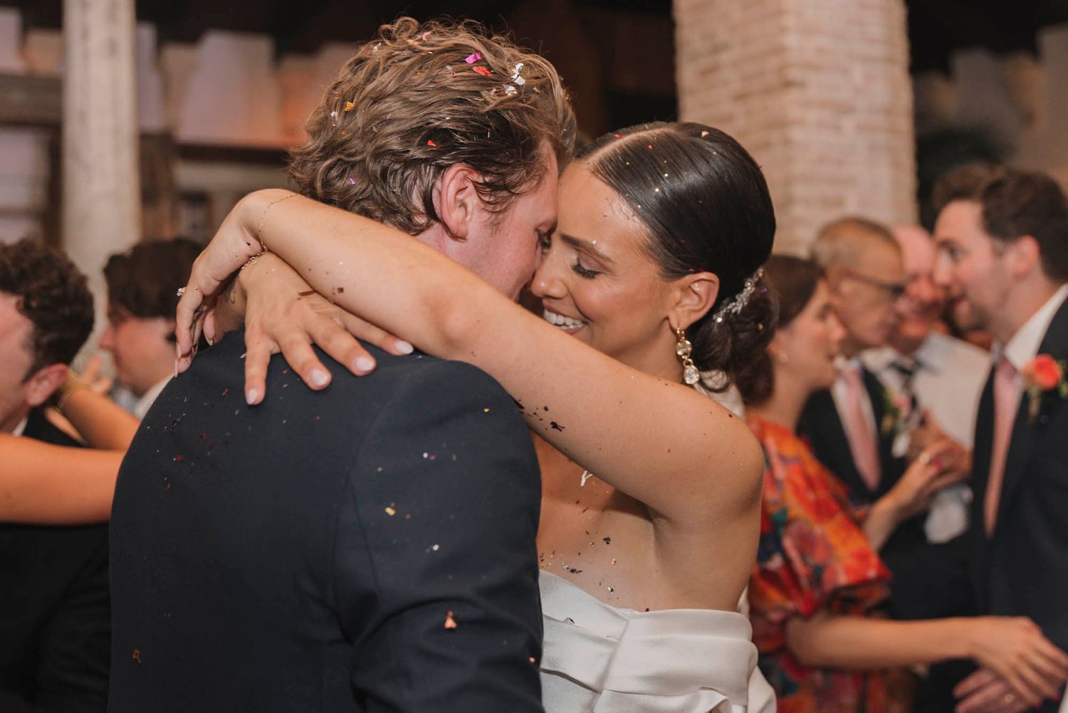 An intimate embrace during a wedding dance on a confetti-covered floor.