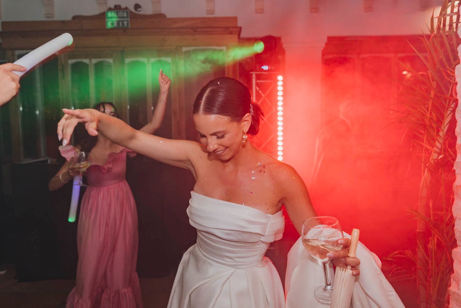 A person in a white wedding dress dances joyfully on the dance floor under red and green lighting.
