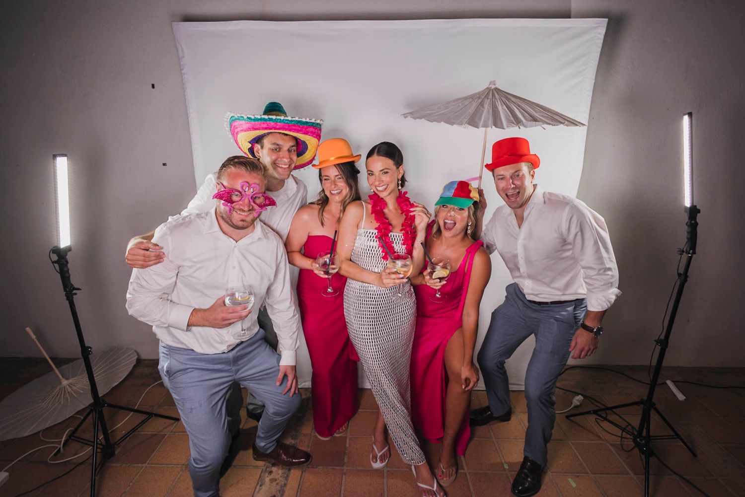 Group photo of party guests in formal attire posing with props against white backdrop and studio lights.