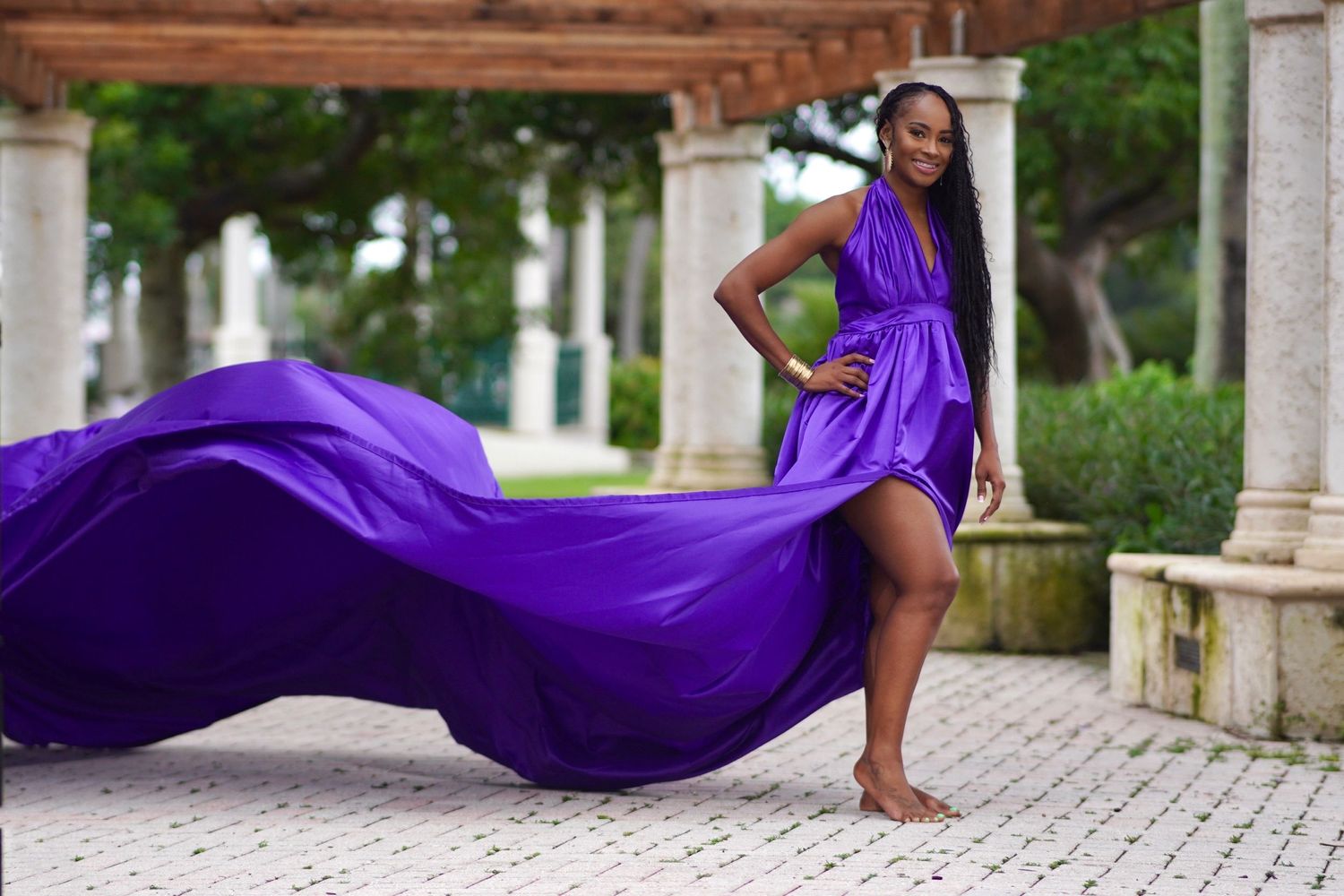 A flowing purple gown with dramatic movement photographed in an elegant outdoor colonnade setting.
