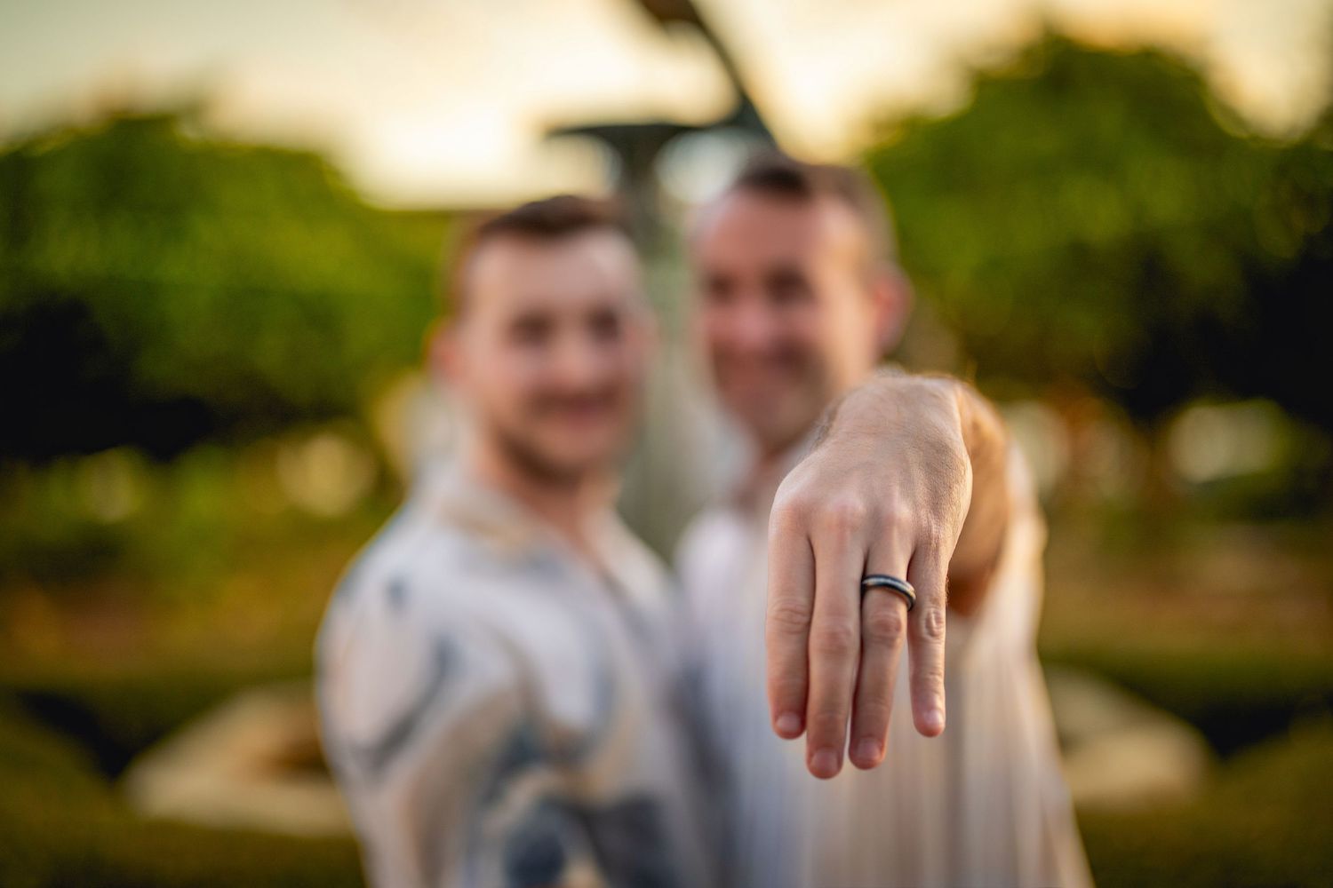 A close-up shot of a hand displaying an engagement ring with a blurred background at sunset.