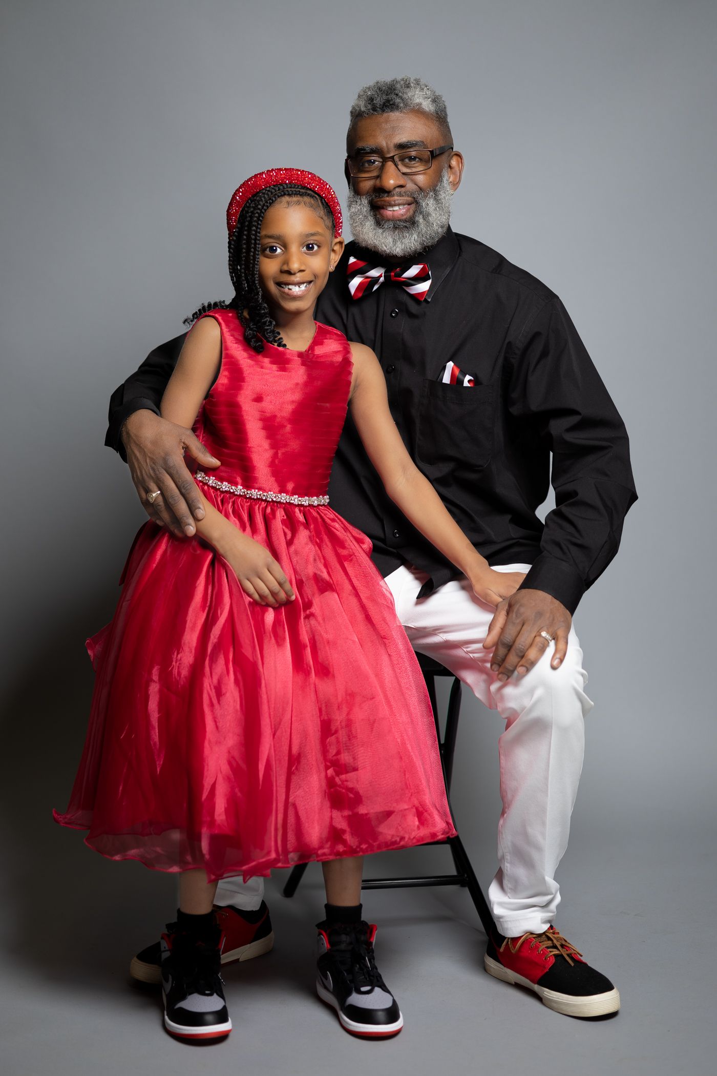 Portrait of duo in matching red and black formal attire against grey background.