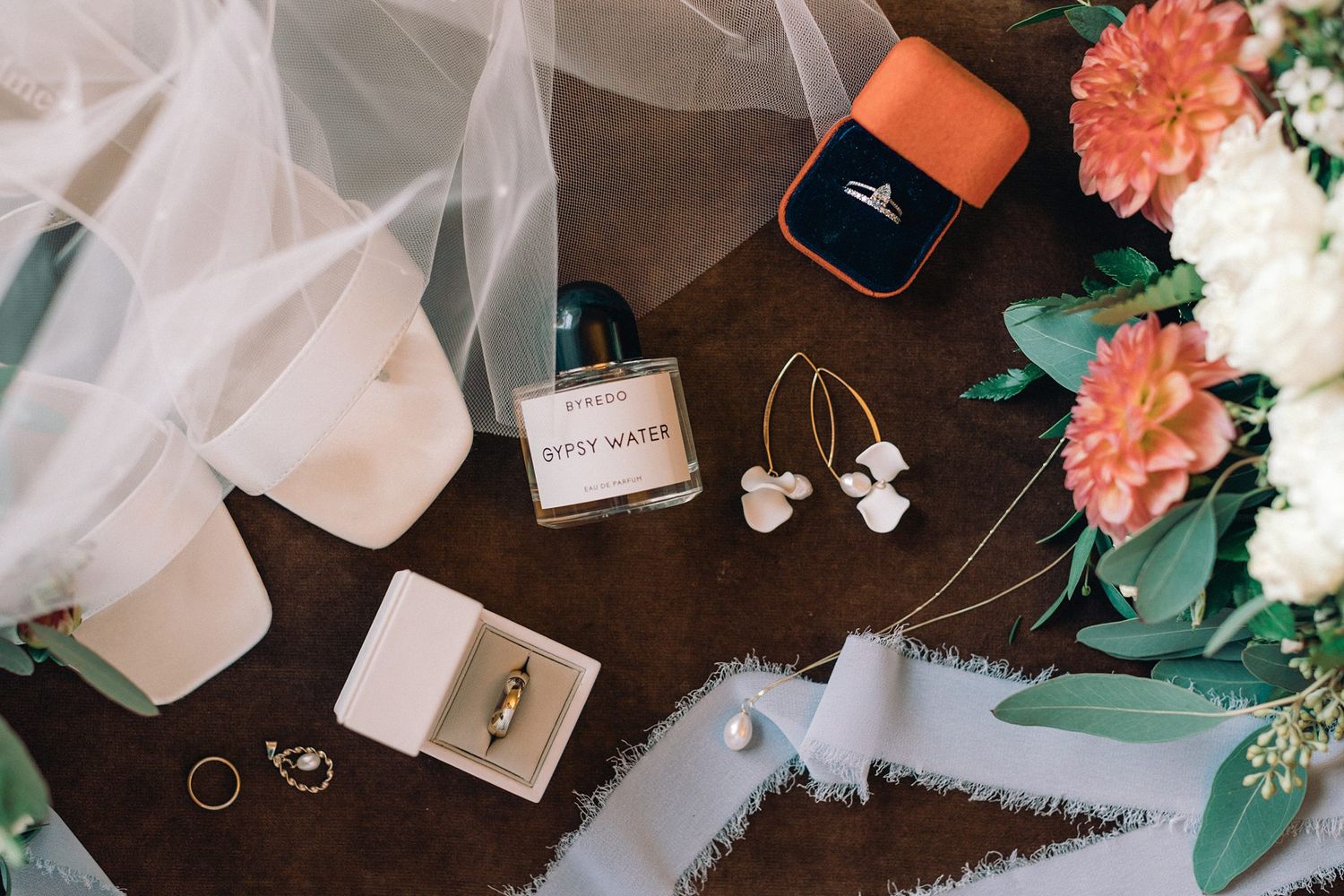 Wedding accessories including perfume, jewellery, veil, and coral flowers arranged on dark brown surface at Whitepoint Resort, Nova Scotia