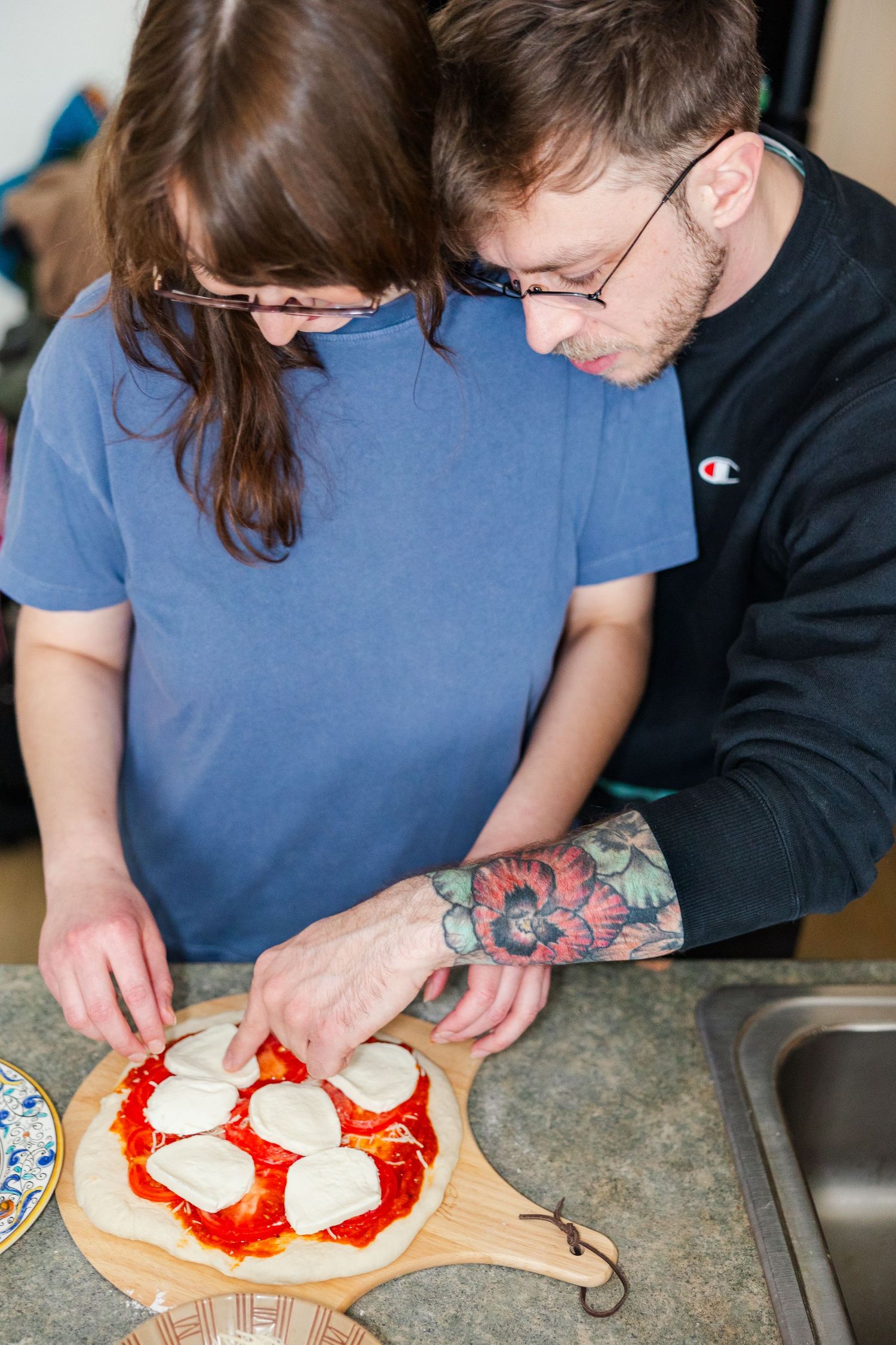 Couple preparing a homemade pizza with fresh mozzarella on wooden cutting board.