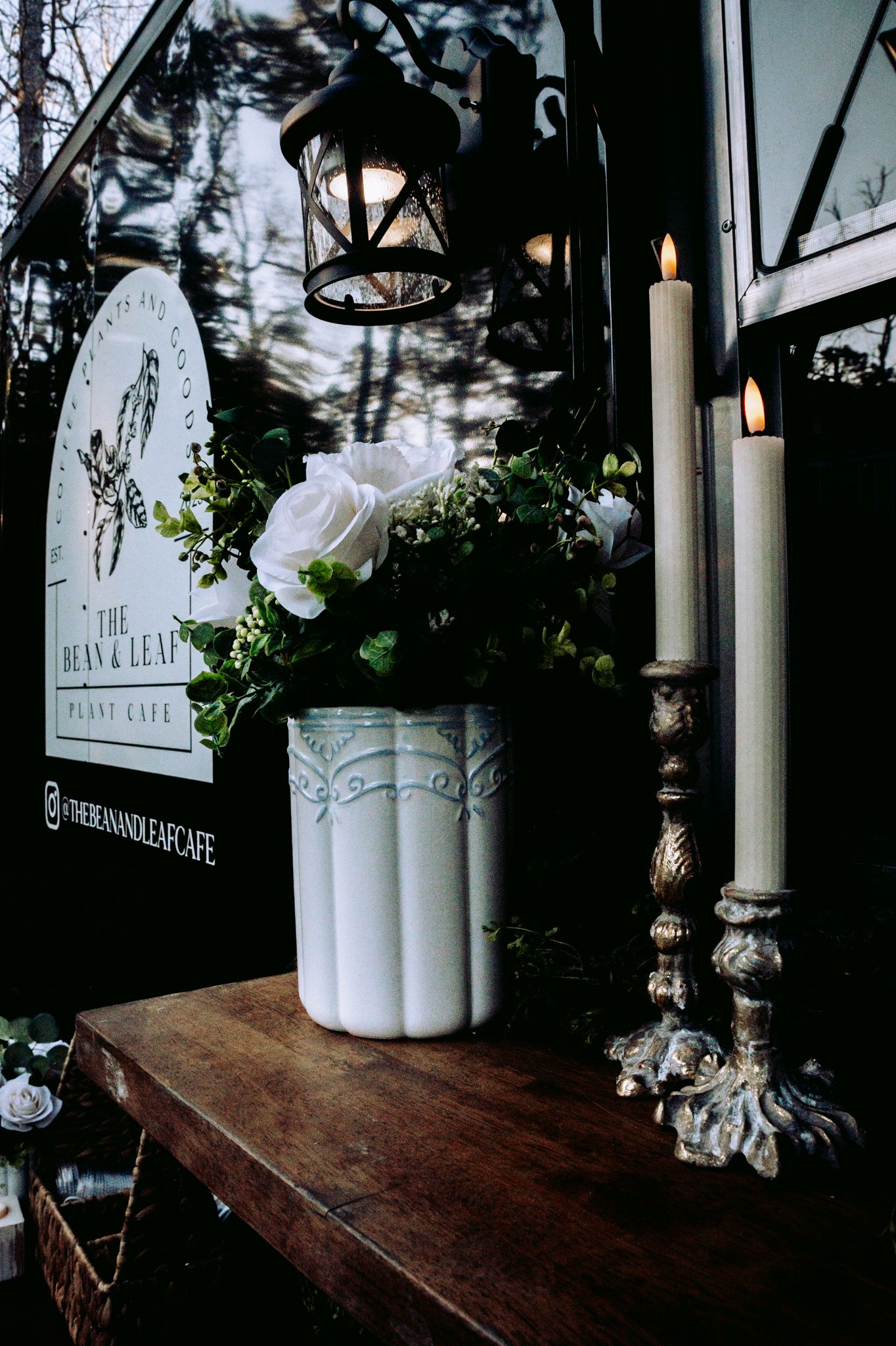 Moody close-up of white roses and candles on rustic wooden surface with vintage lantern.