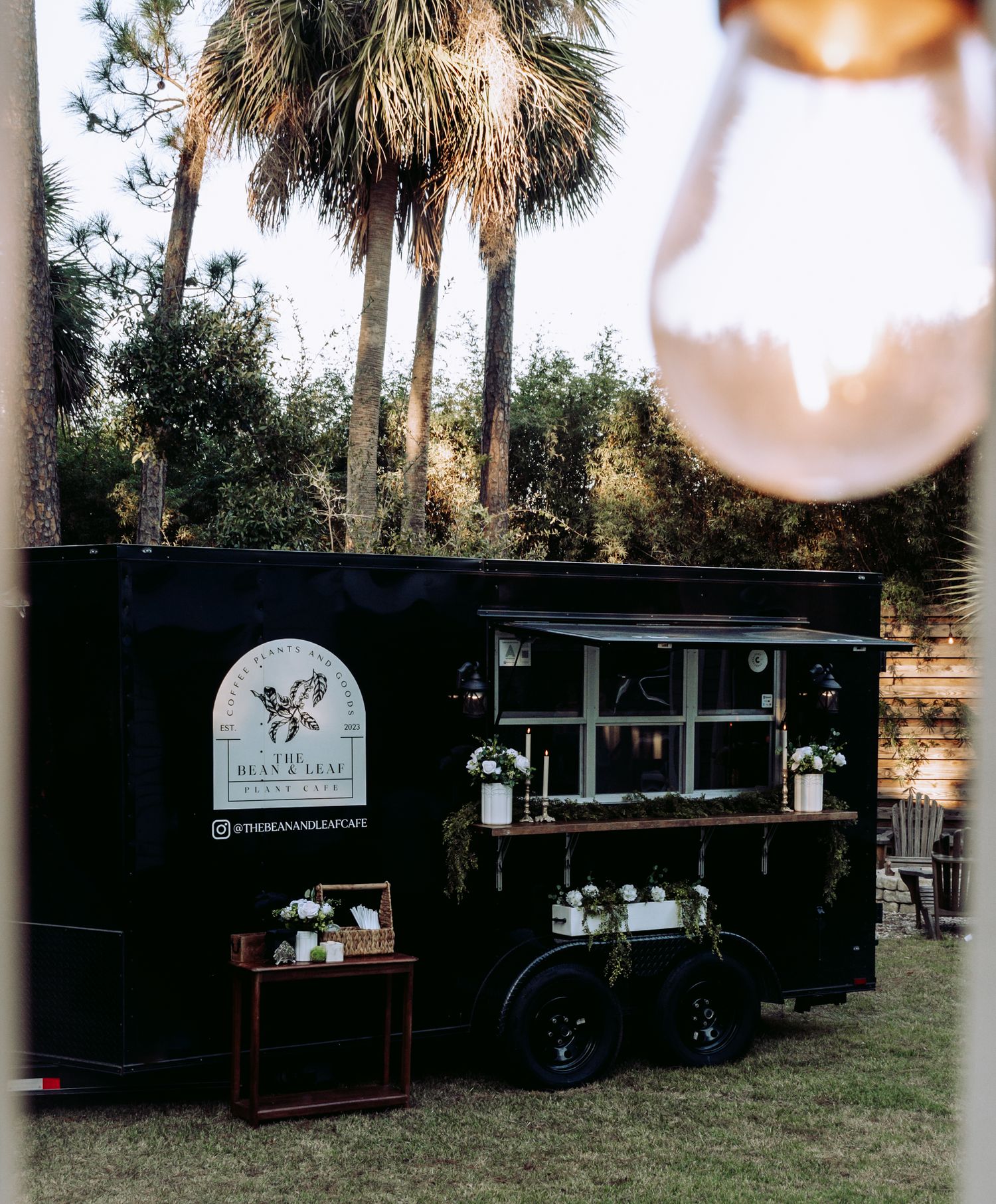 Black mobile coffee cart with The Bean & Leaf branding surrounded by palm trees at sunset.